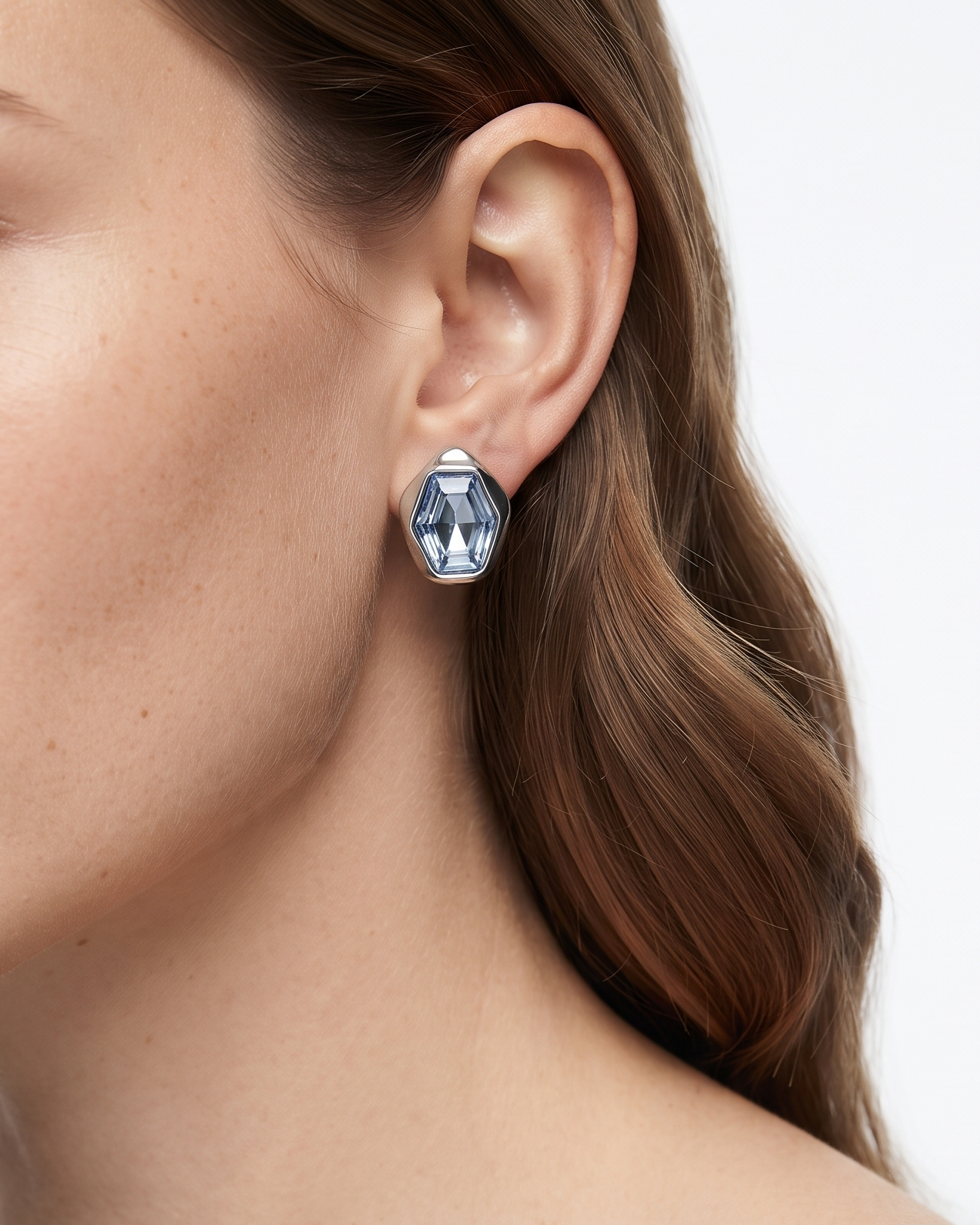 Close-up of a woman wearing a geometric silver earring with clear faceted stones, shown against a clean white background.