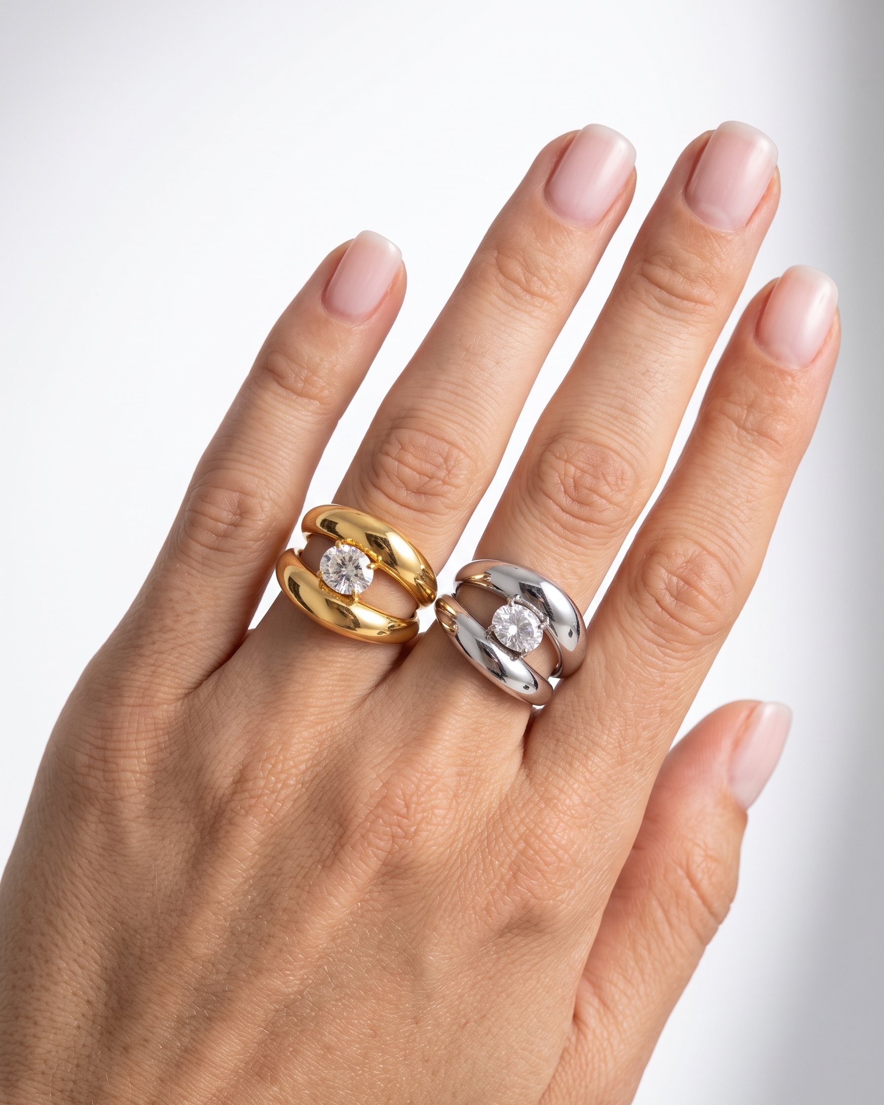 Hand wearing two rings, one gold and one silver, on a light background
