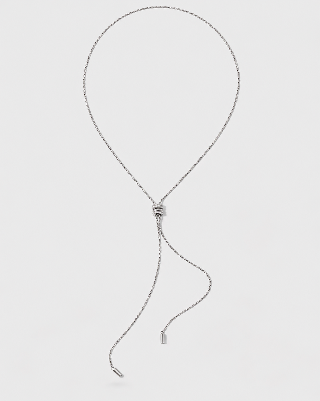 A silver-toned adjustable necklace with a delicate chain, a central sliding bead clasp, and two dangling chain tails with small metal tags, shown on a light gray background.