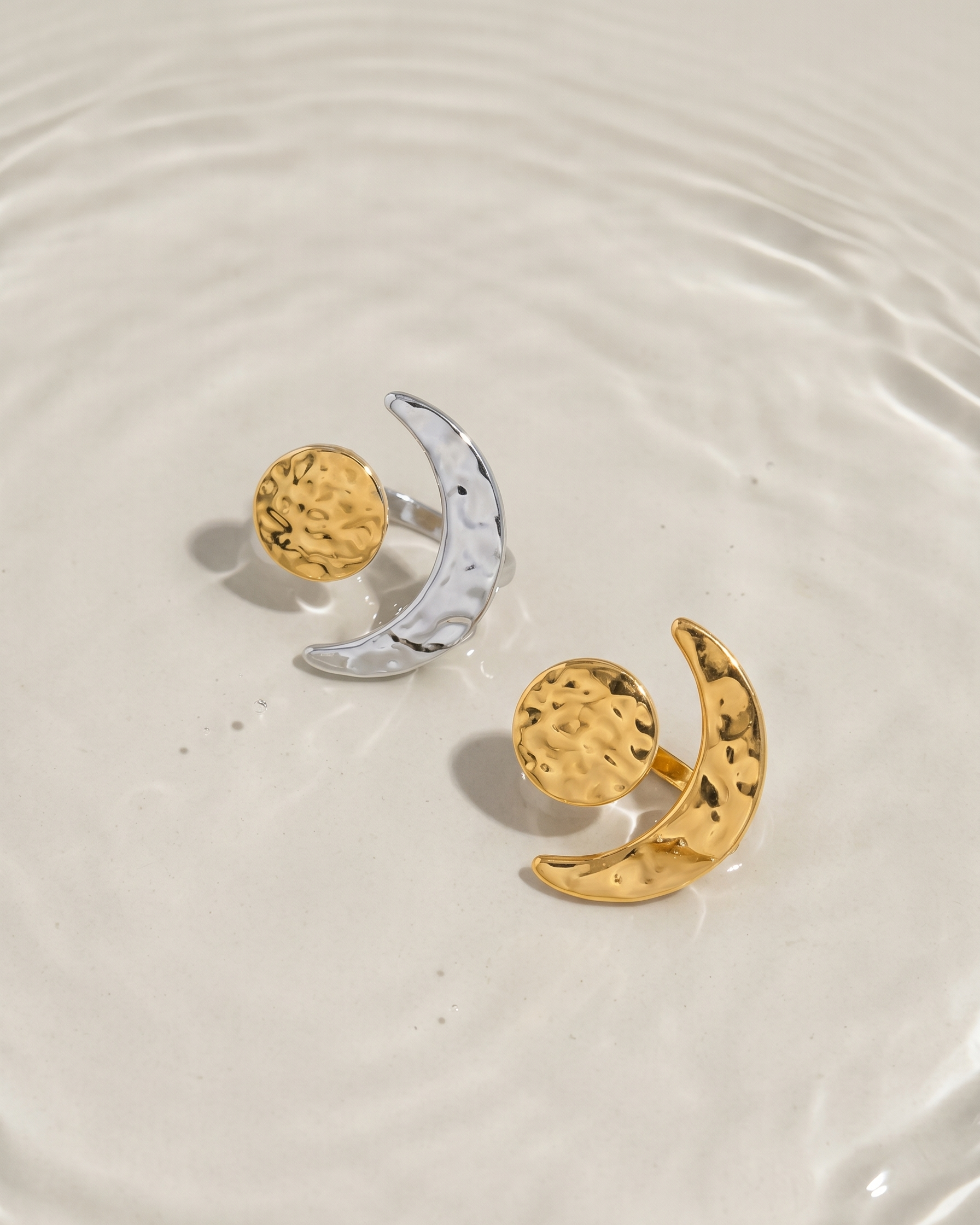 Two gold and silver earrings on a reflective surface