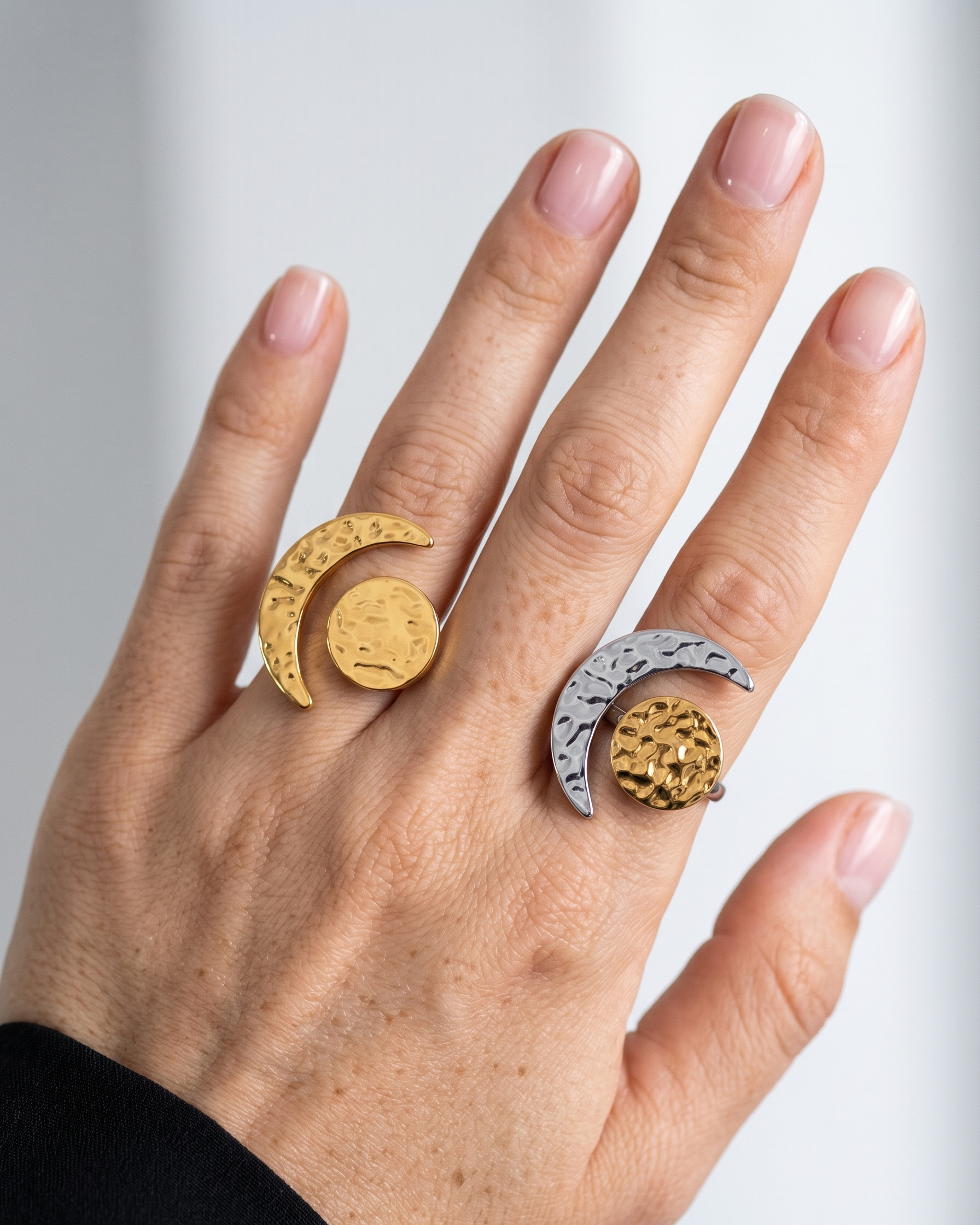 Hand wearing two rings with moon designs on a light background
