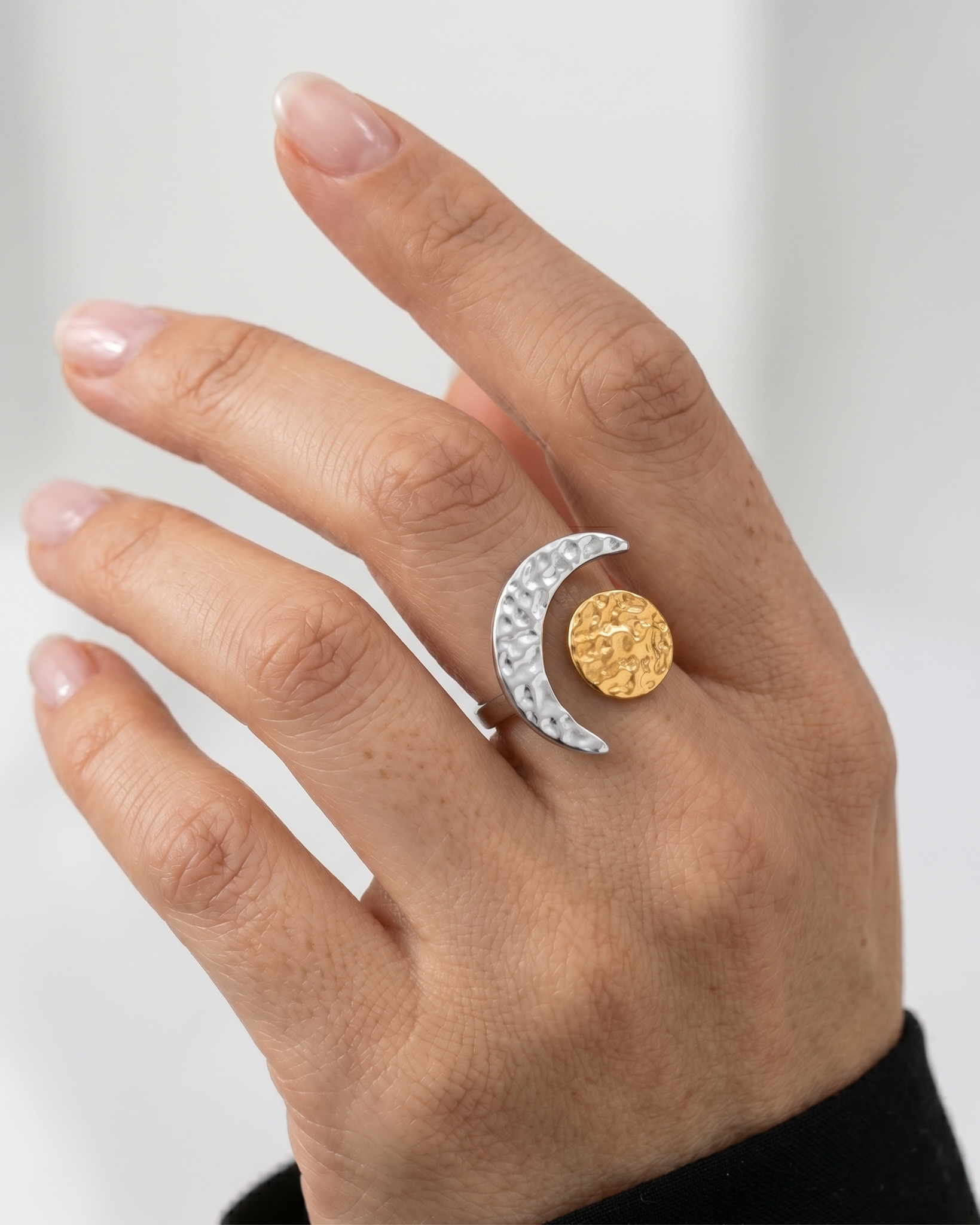 Hand wearing a silver ring with a gold coin design on a light gray background