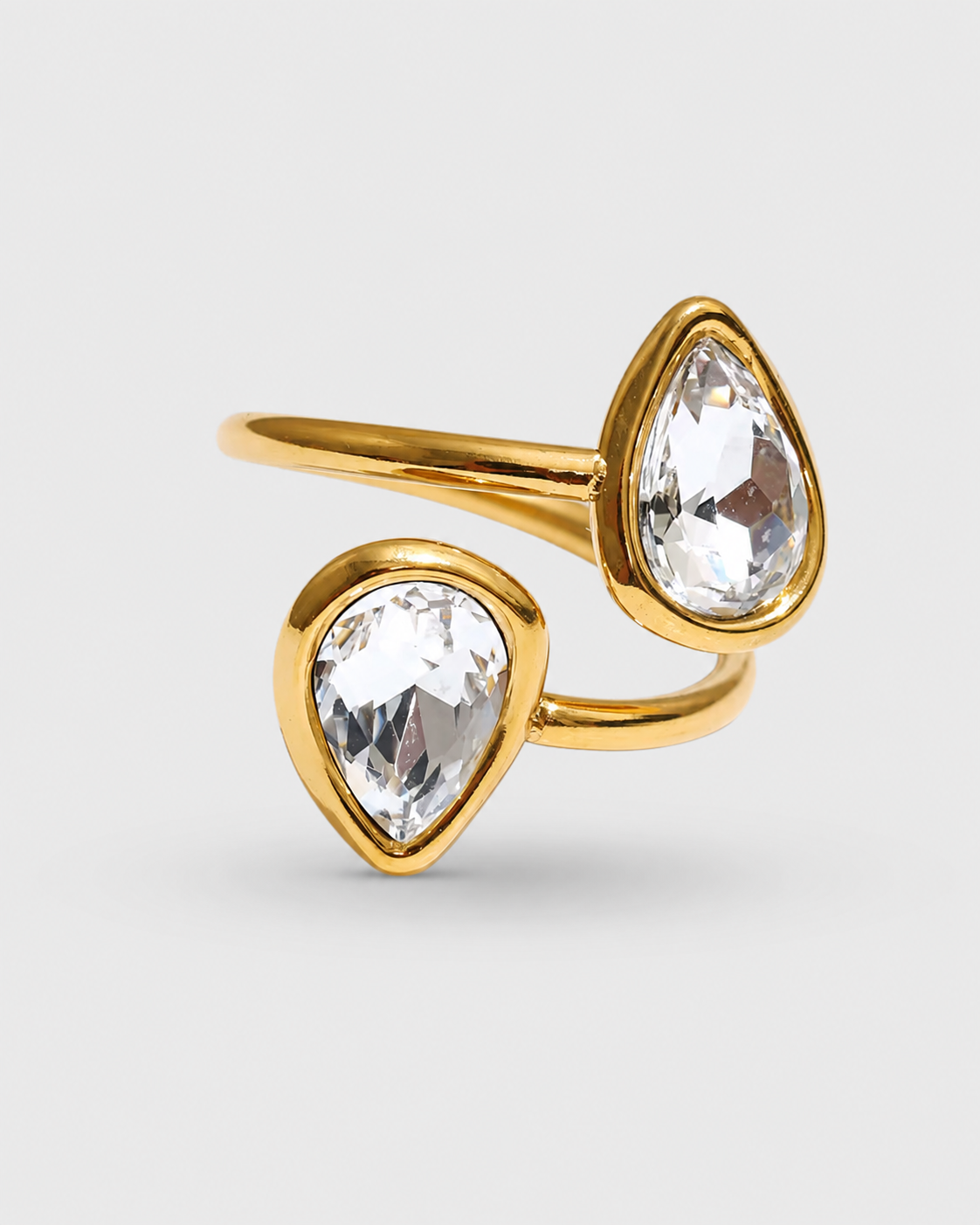 A gold ring with two teardrop-shaped clear gemstones in bezel settings, shown on a light gray background.