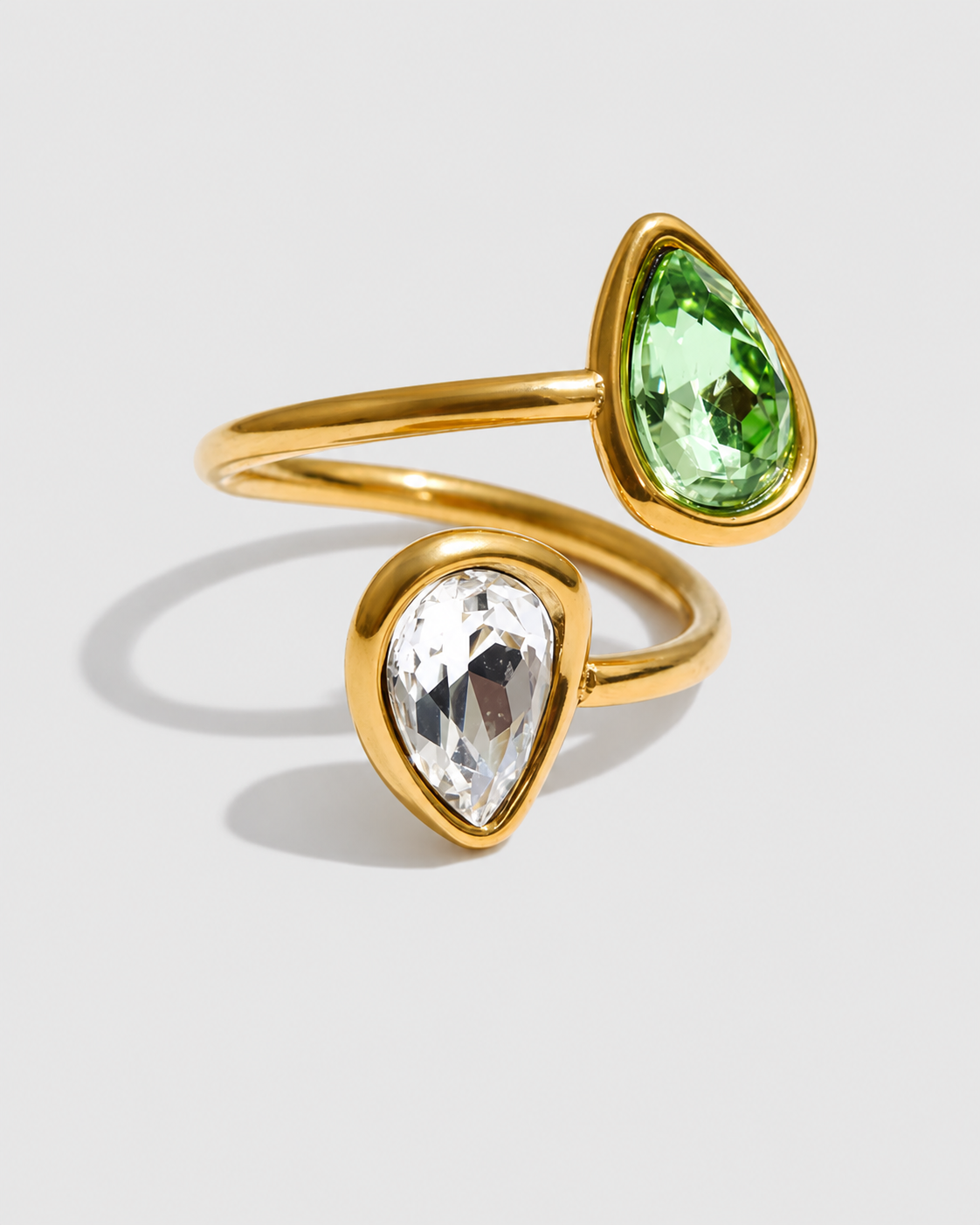 A gold wrap ring featuring two teardrop-shaped gemstones, one green and one clear, set in a polished gold band on a light gray background.