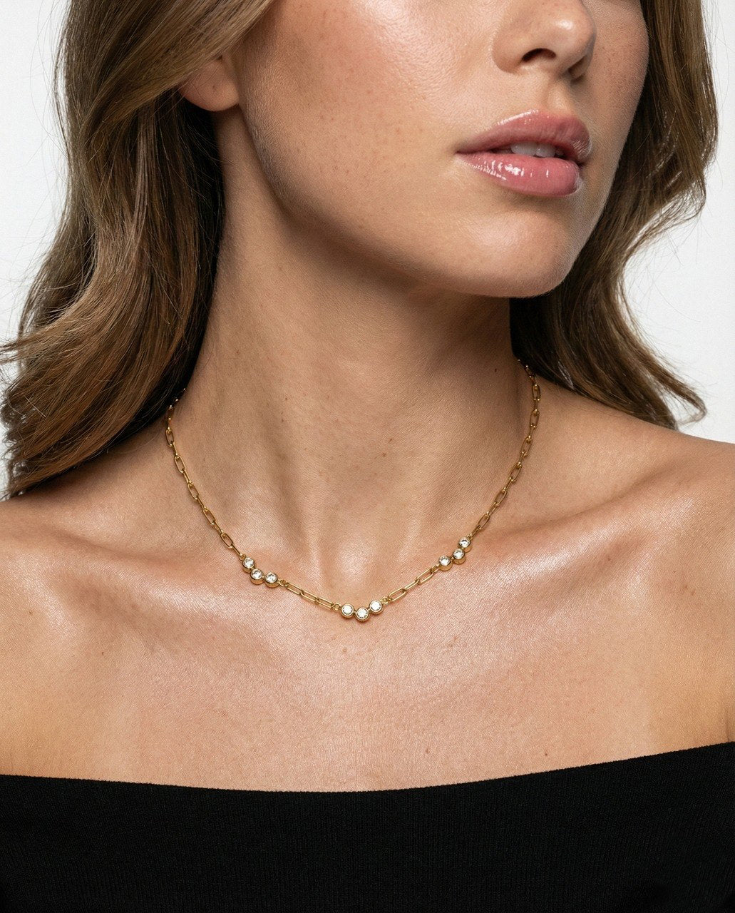 Close-up of a woman wearing a gold necklace against a neutral background