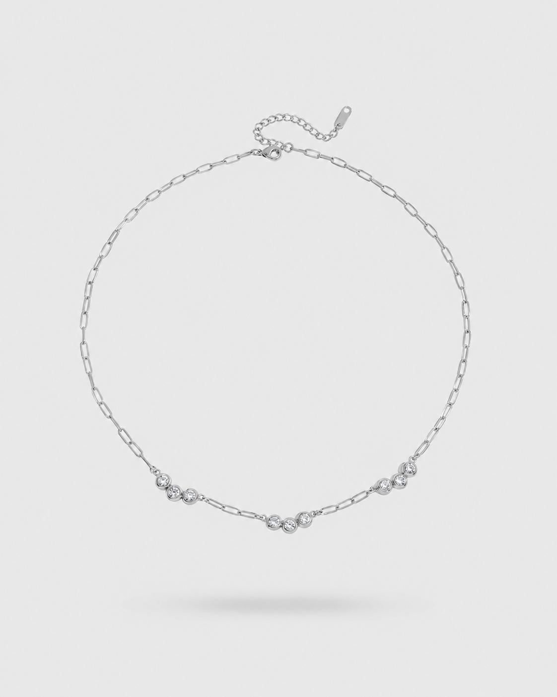 A delicate silver chain necklace with three small floral clusters and a central heart-shaped charm, displayed on a light gray background.