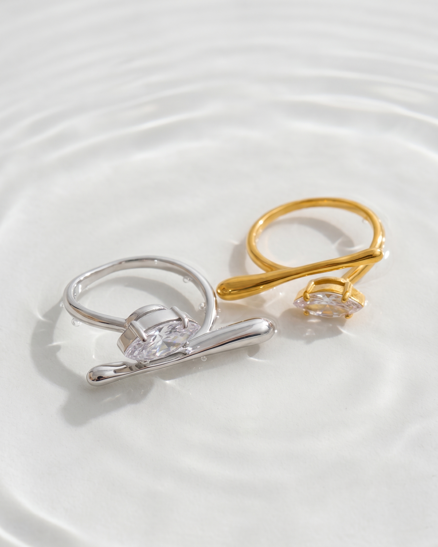 Two rings, one silver and one gold, on a white surface with water effect