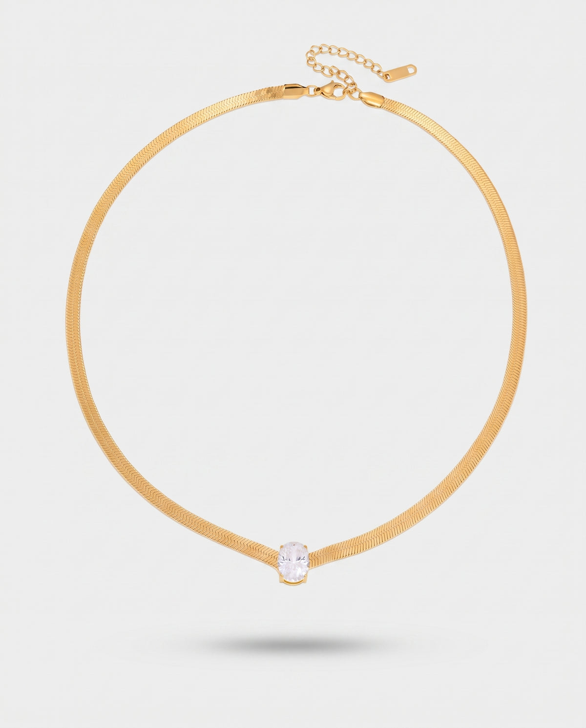 A gold-toned snake chain choker necklace with a single bezel-set clear oval gemstone at the center, shown on a light gray background.