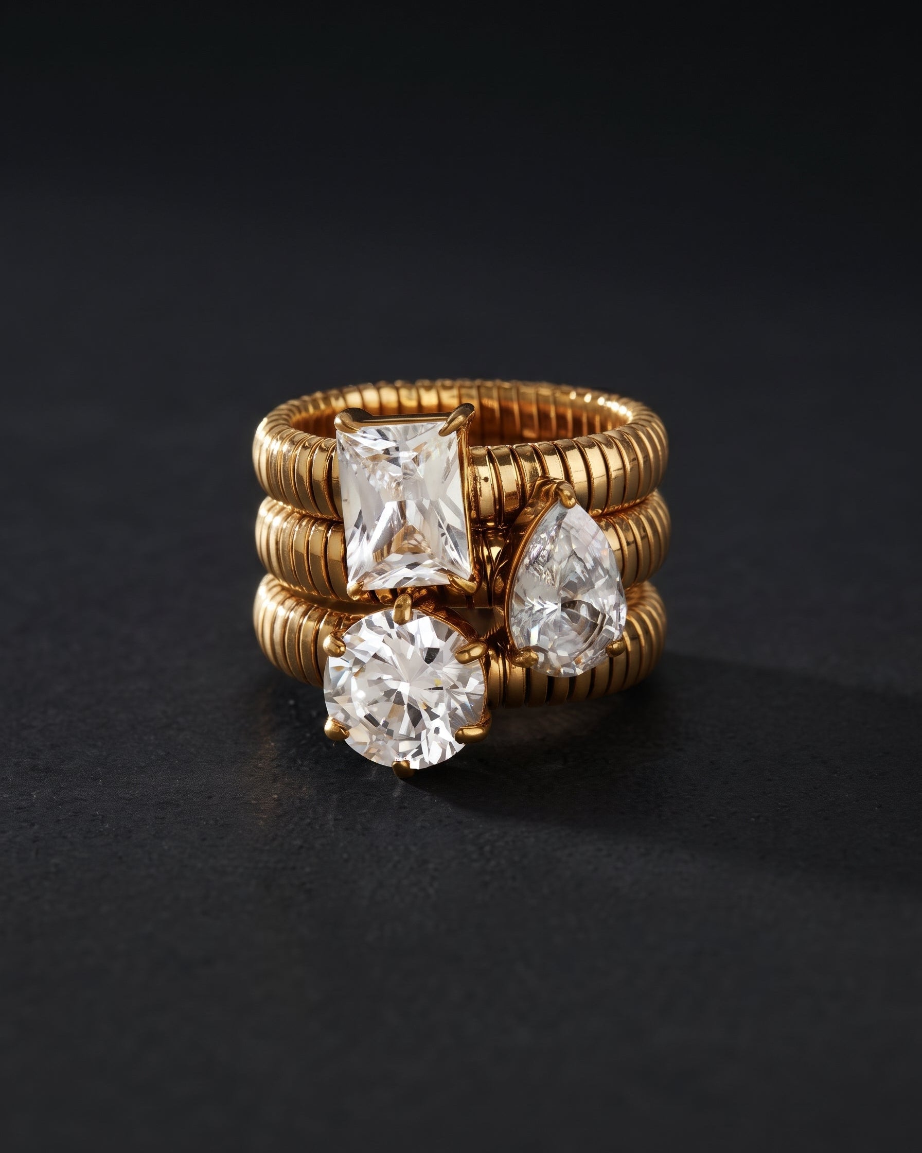 A gold ring with three diamond-cut stones in different shapes, displayed on a dark textured background.