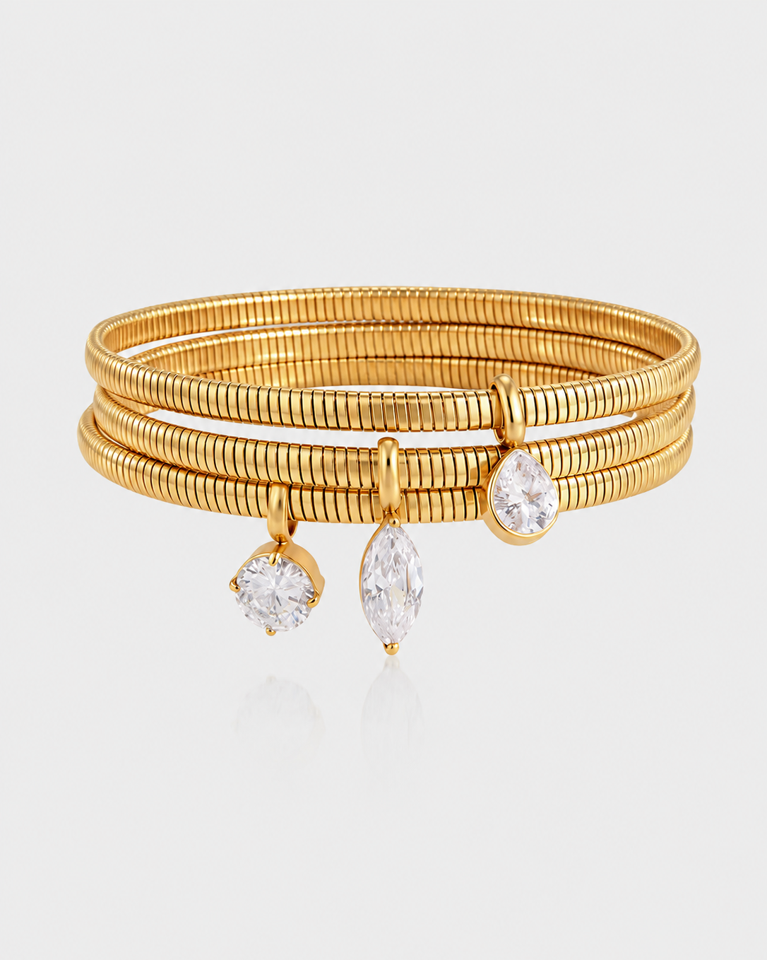 A gold multi-band bangle bracelet featuring three dangling pear-cut clear gemstones, displayed on a light gray reflective surface.