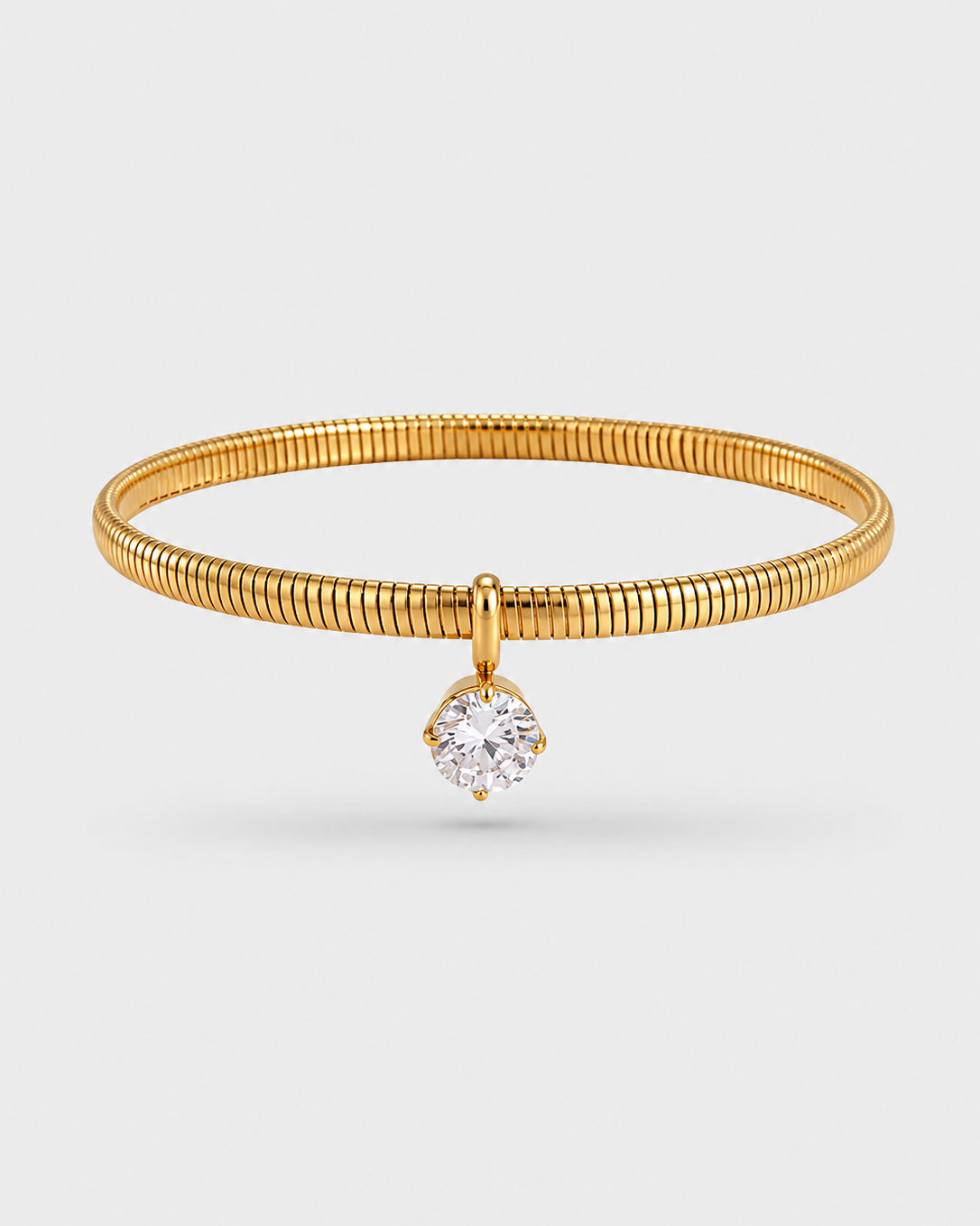 A gold snake-bone bangle bracelet with a single round-cut clear gemstone pendant, shown on a light gray background.