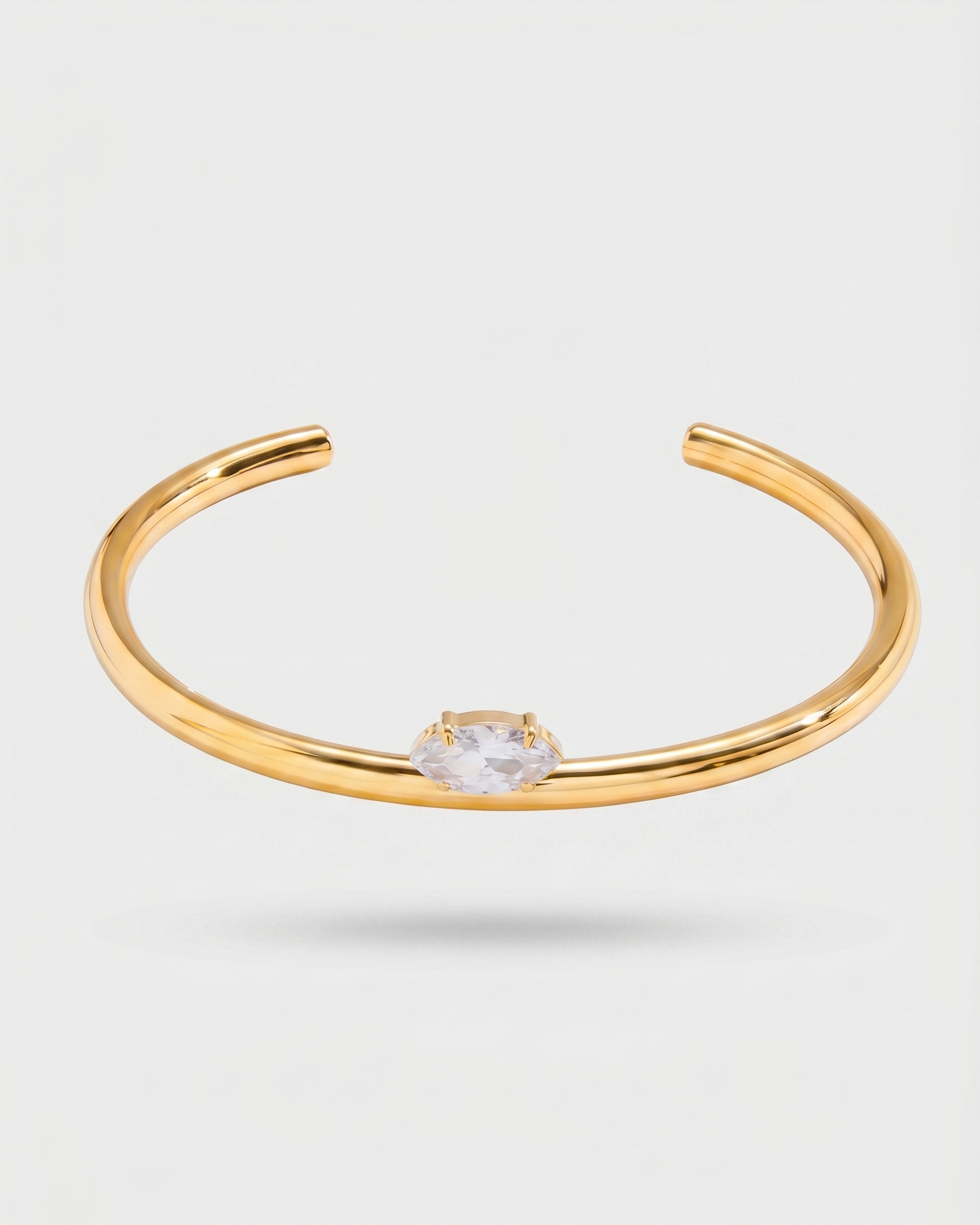 Gold bracelet with a clear gemstone on a light gray background