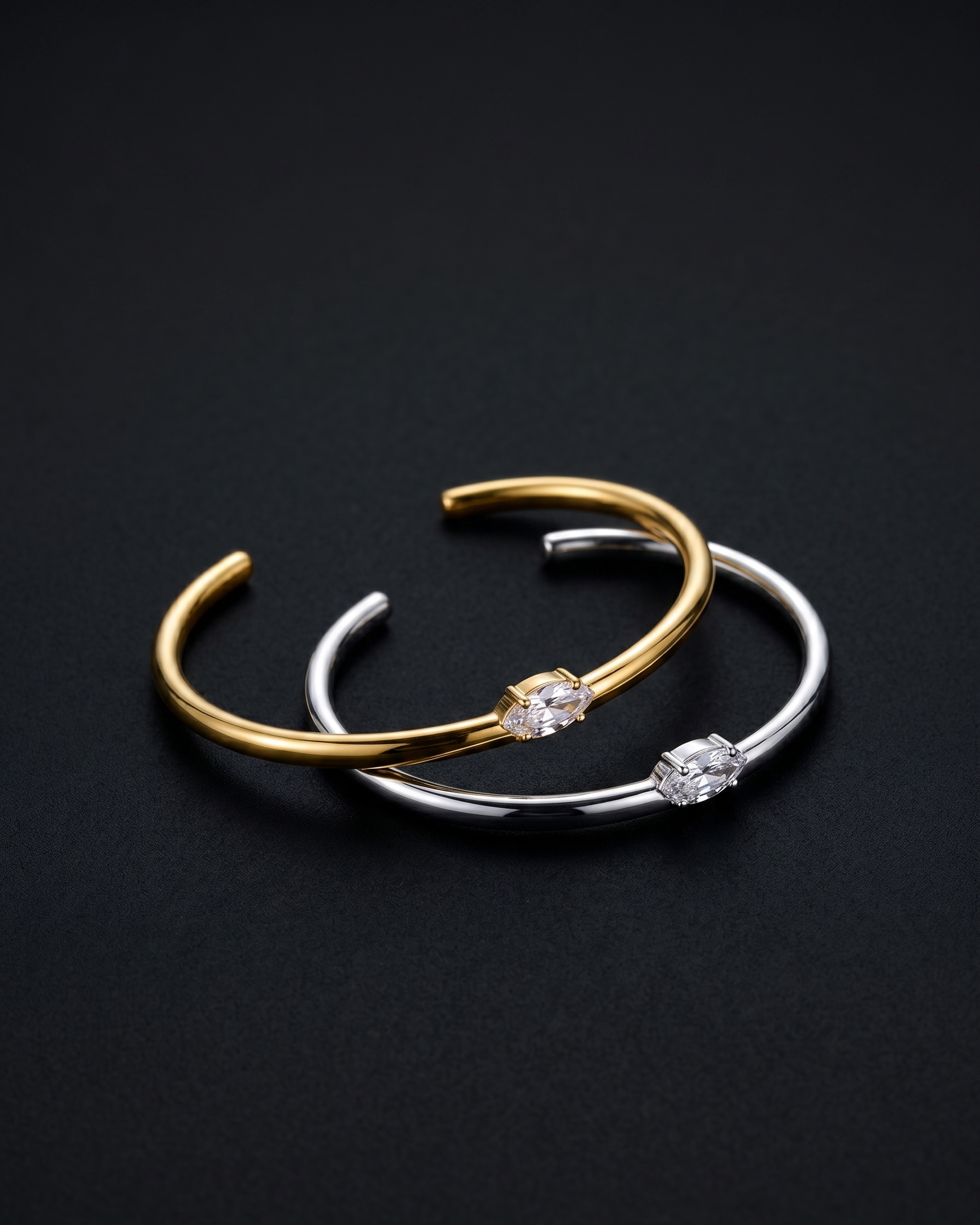 Two gold and silver bangle bracelets with embedded stones on a black background