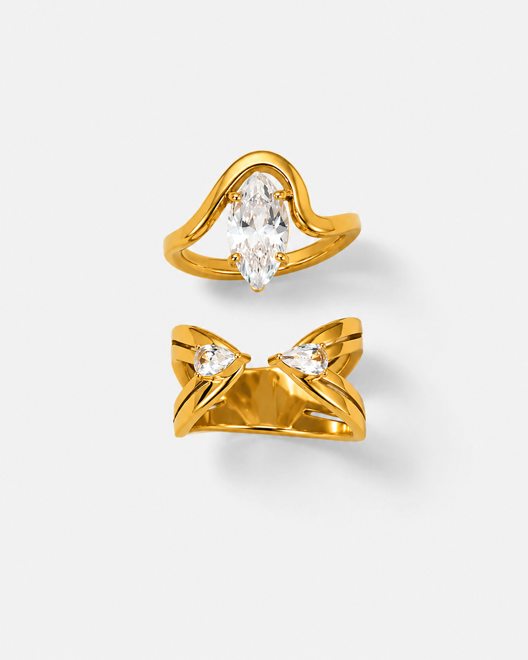Two gold rings displayed on a light gray background. The top ring features a curved gold band with a marquise-cut clear gemstone.