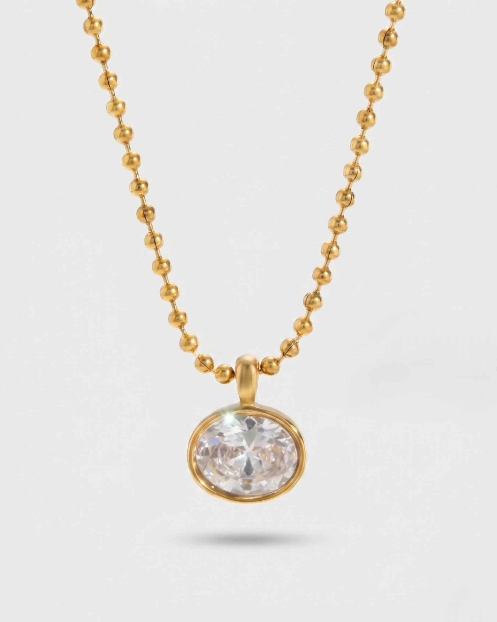 Gold necklace with a clear gemstone pendant on a light gray background