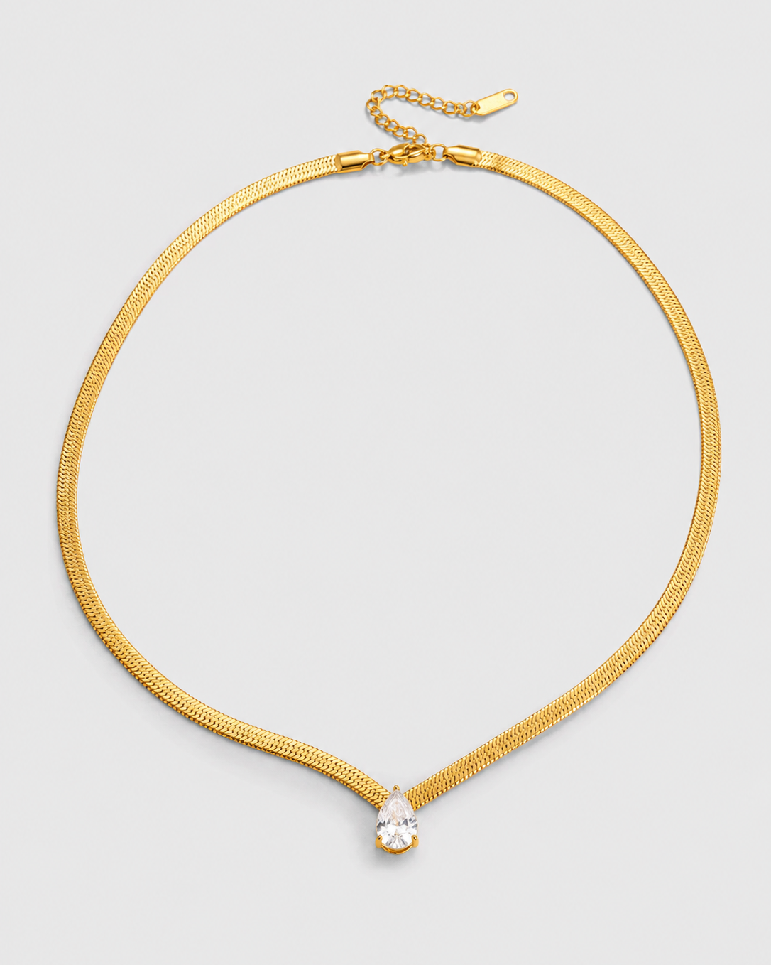 A gold-tone snake chain choker necklace with a small clear teardrop crystal pendant, displayed on a light gray background.