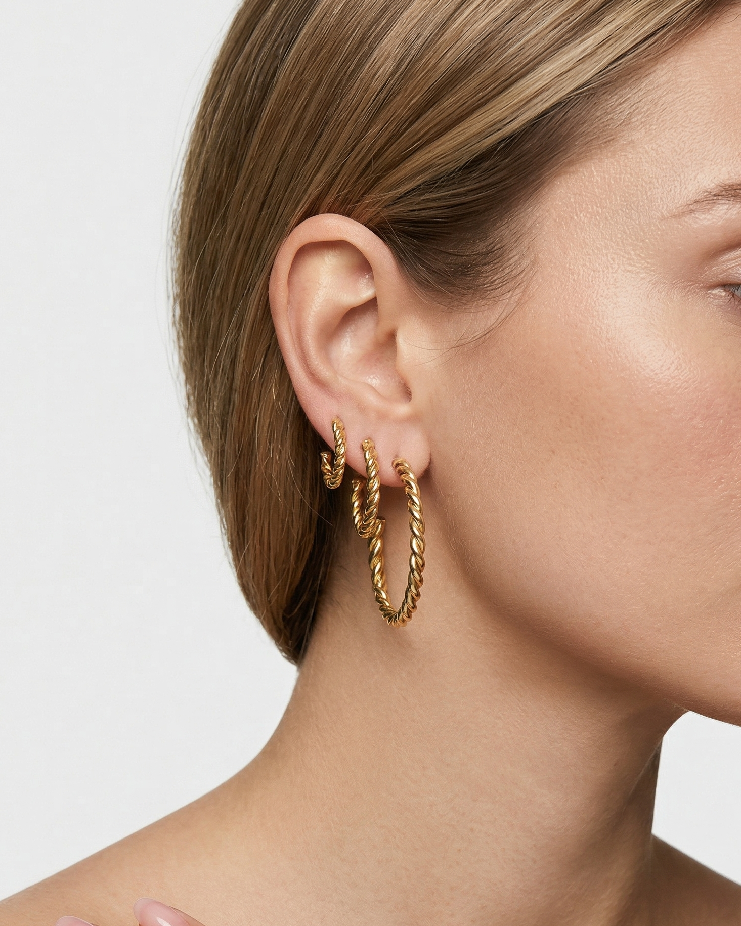 Close-up of a woman wearing gold hoop earrings with a plain background