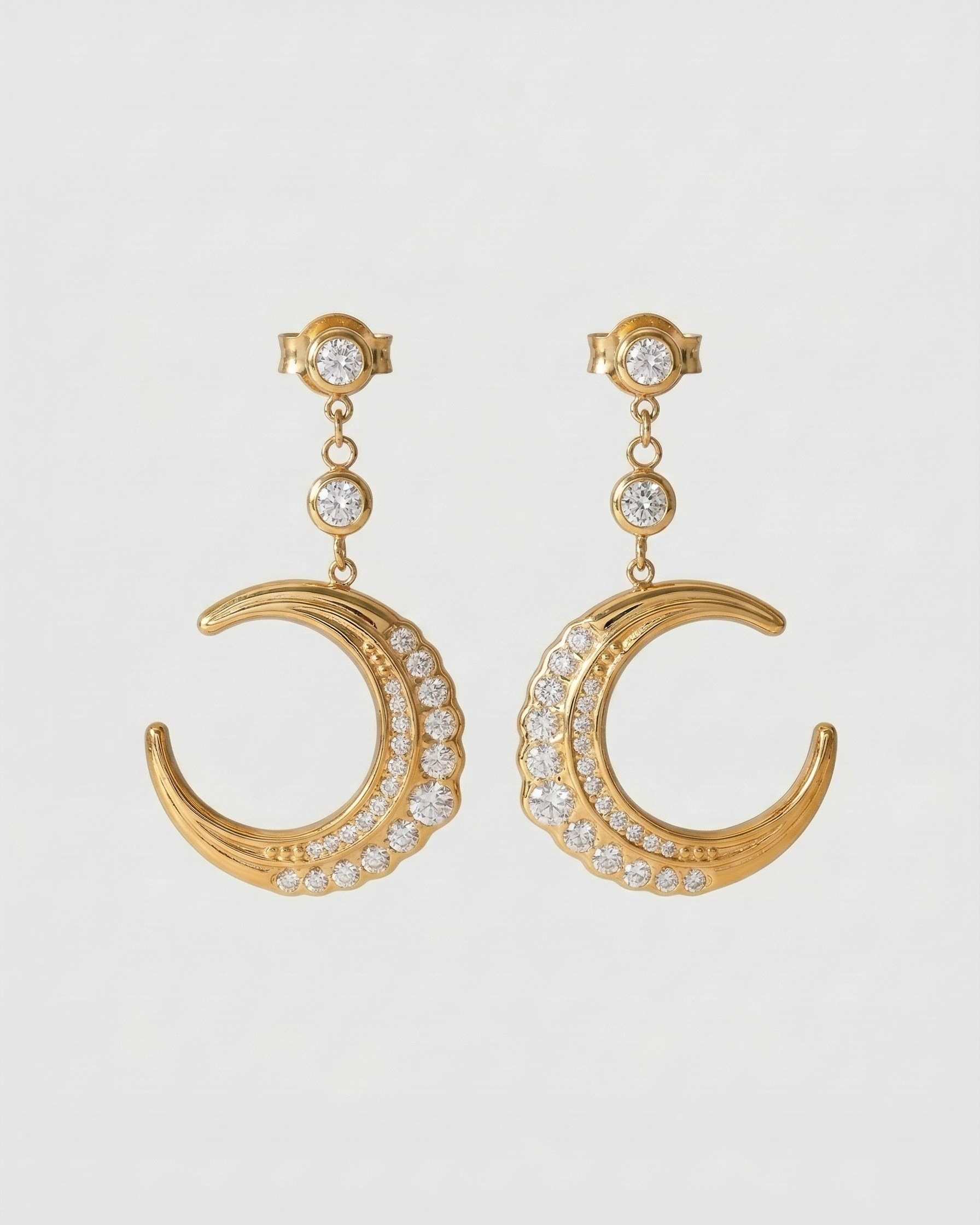 Gold crescent moon earrings with clear stones on a light gray background