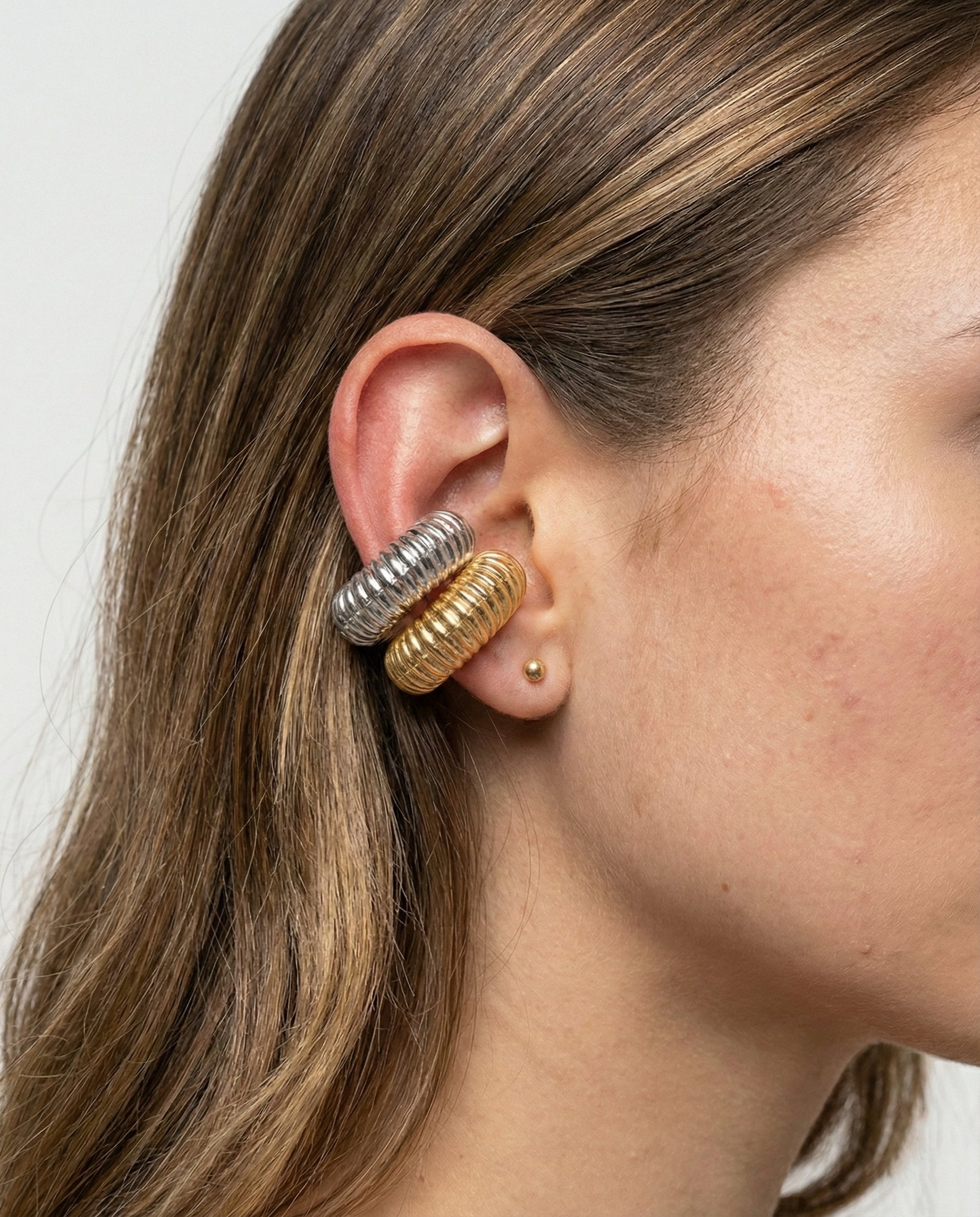 Close-up of a person wearing two gold hoop earrings with a plain background