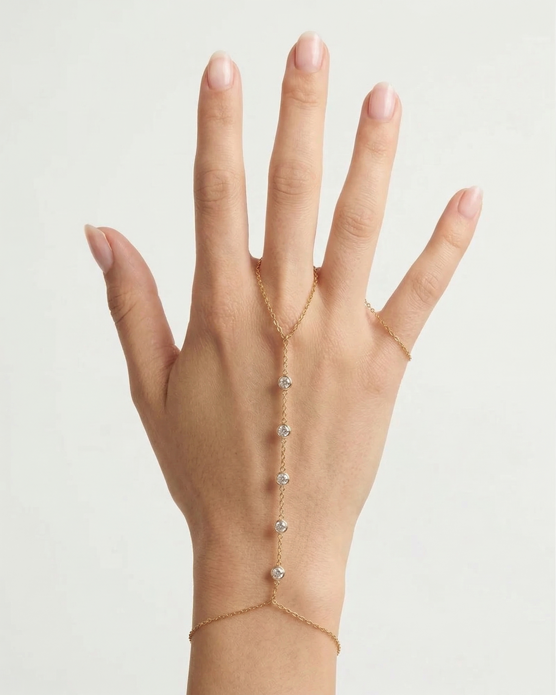 Hand wearing a delicate gold bracelet with small stones on a plain background