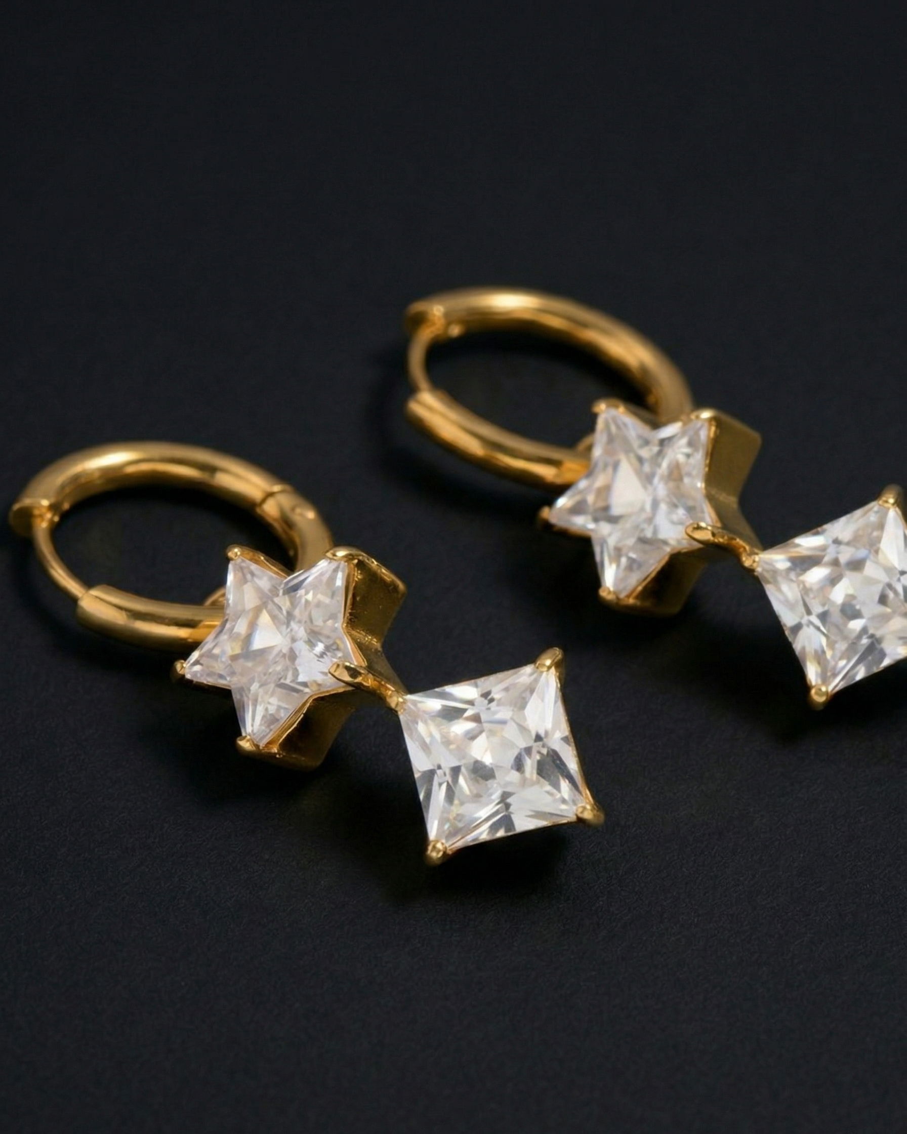 Gold hoop earrings with star-shaped diamond-like stones on a black background