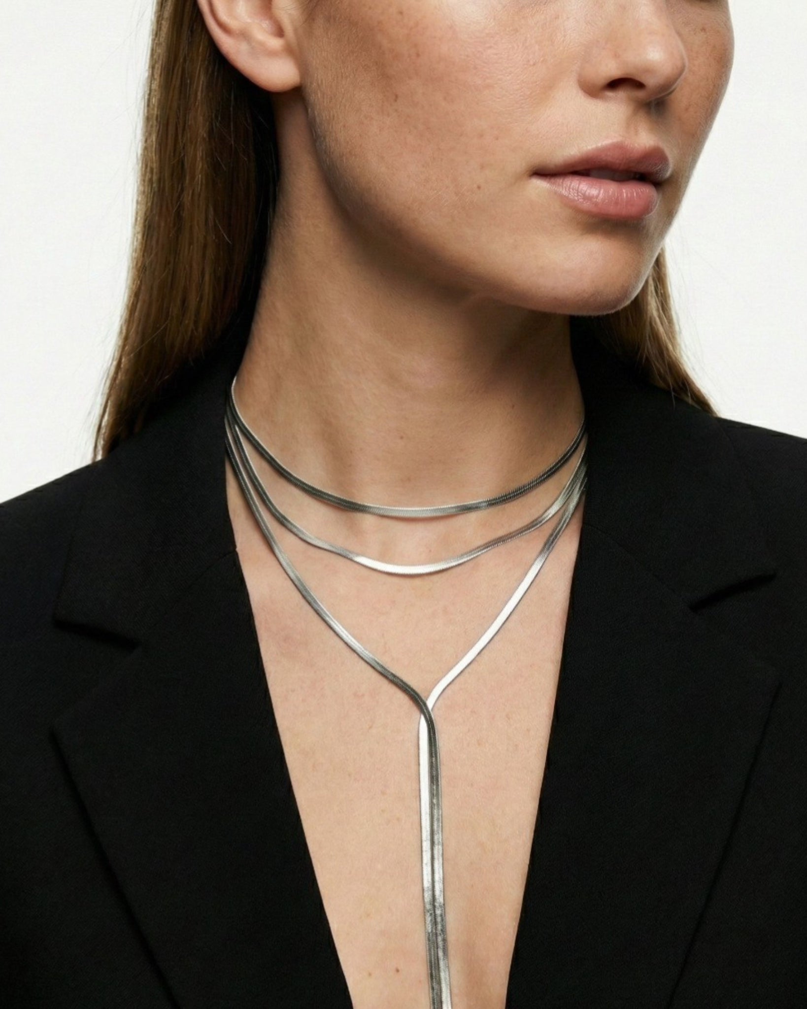 Woman wearing a silver necklace with a plain background