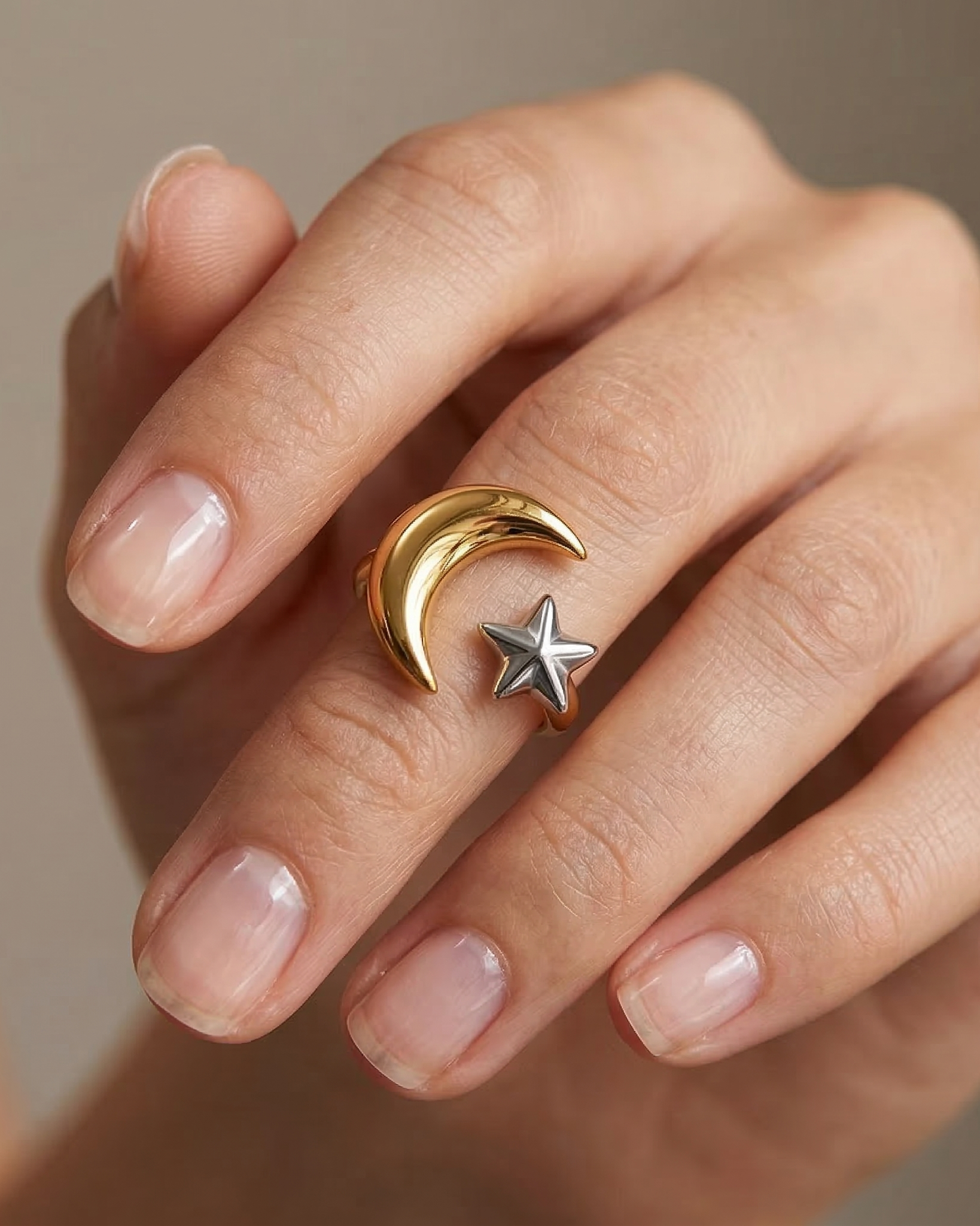 Gold ring with moon and star design on a hand against a neutral background
