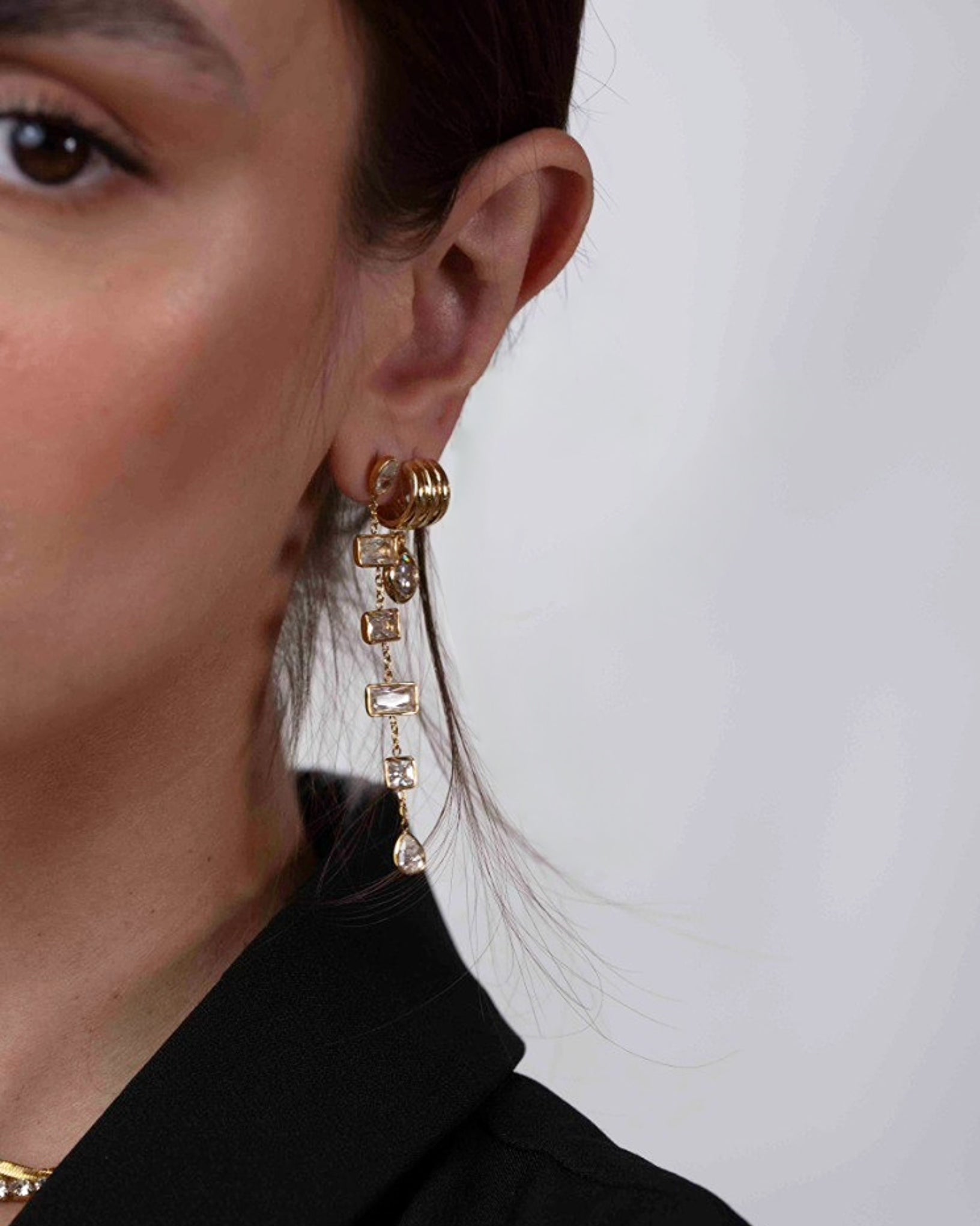 Close-up of a person wearing gold chain earrings with a white background