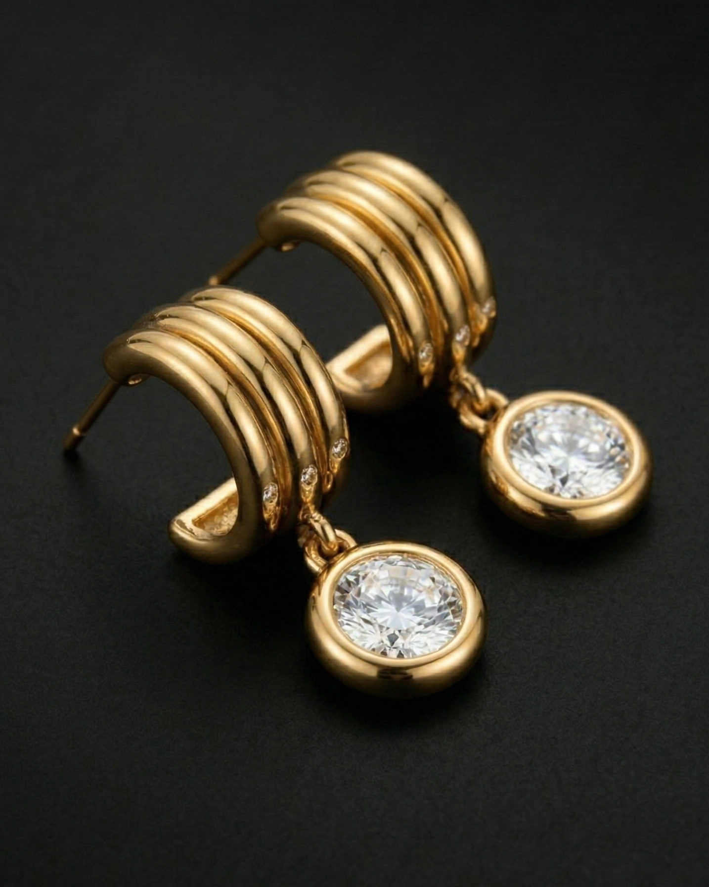 Gold earrings with circular designs and clear gemstones on a dark background