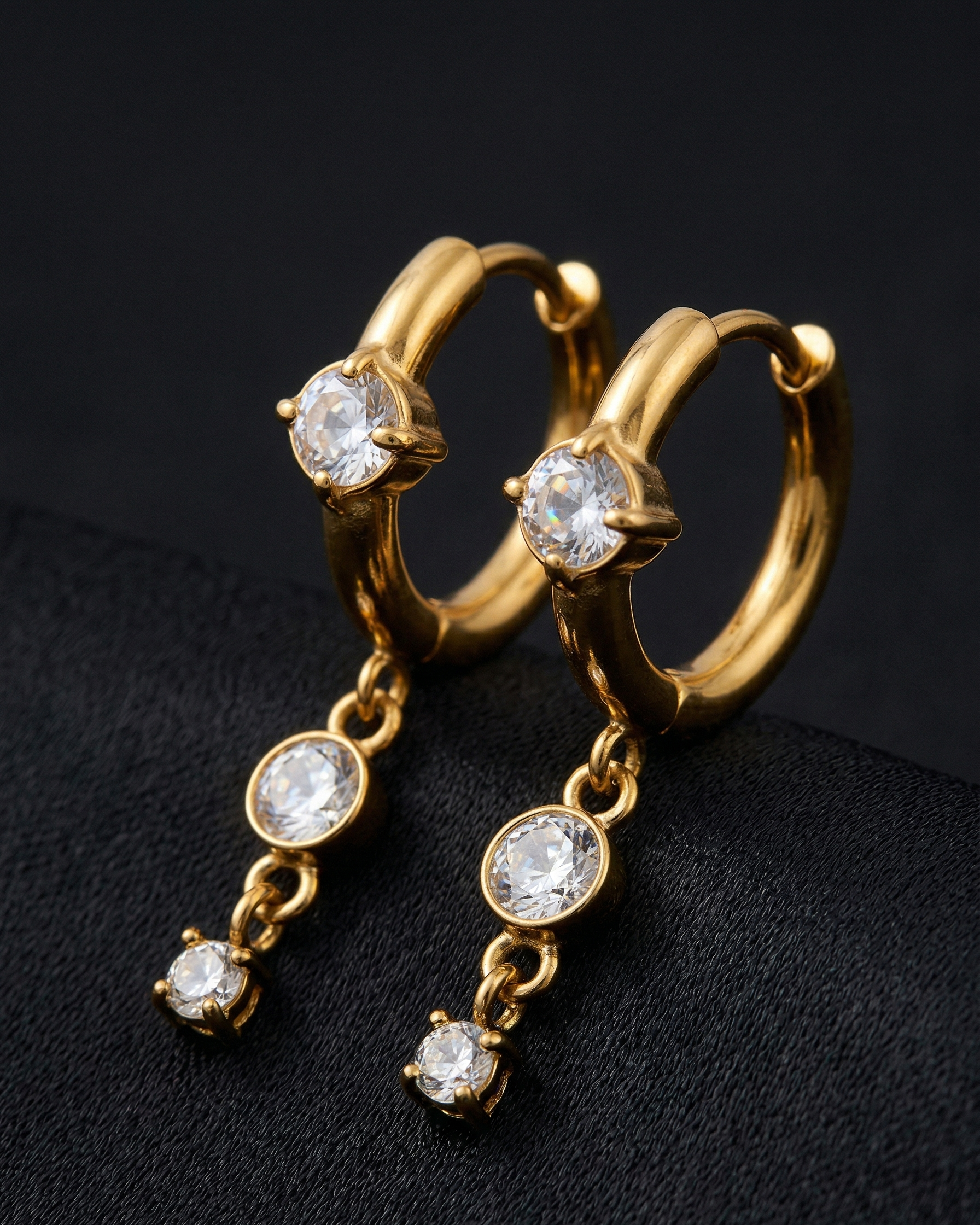 Gold hoop earrings with diamond-like stones on a black background