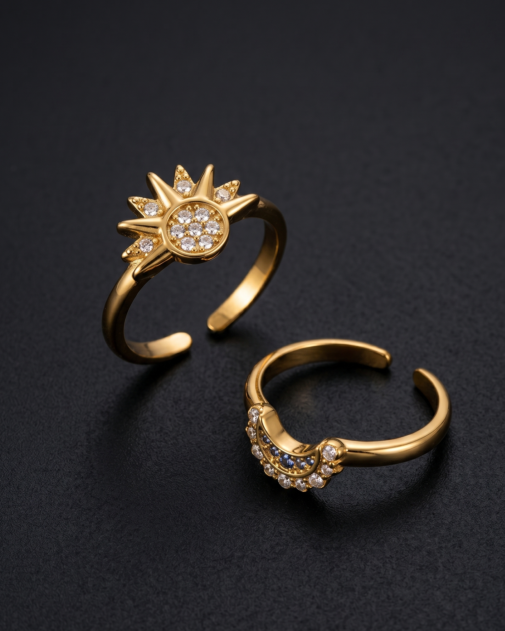 Two gold rings with sun and star designs on a black background