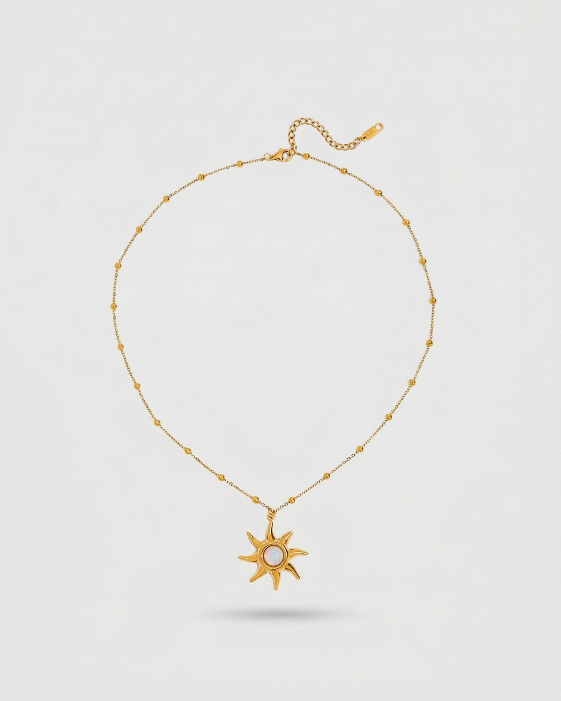 Gold necklace with a sun-shaped pendant on a light gray background