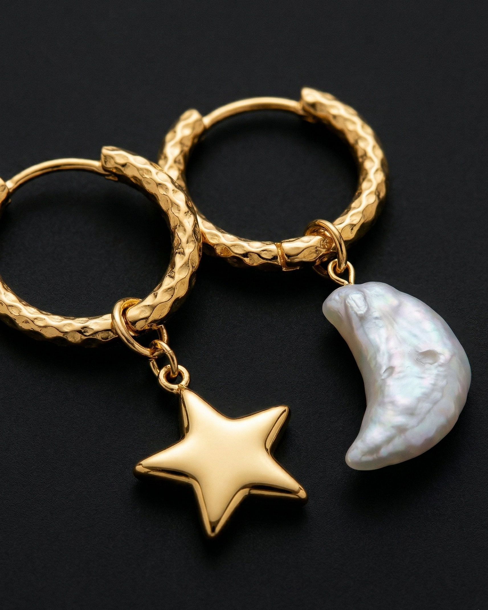 Gold hoop earrings with star and moon charm on a black background