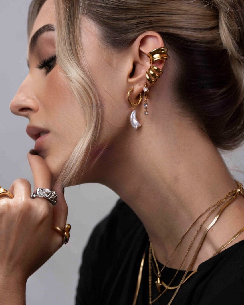 Close-up of a woman wearing gold earrings and necklaces with a neutral background