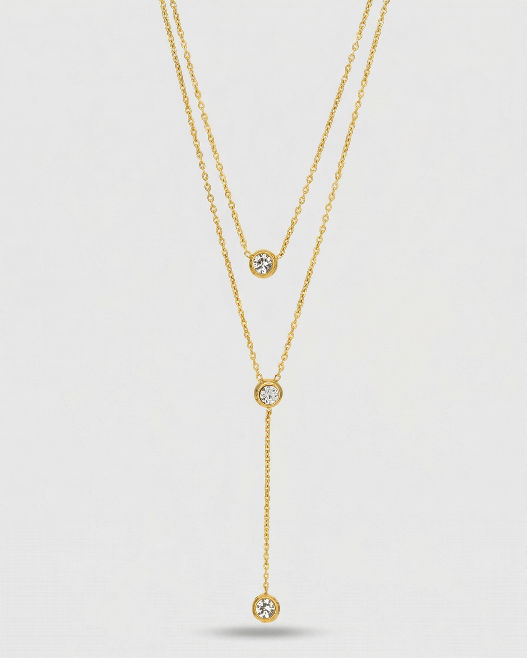 Gold necklace with three diamond pendants on a light gray background