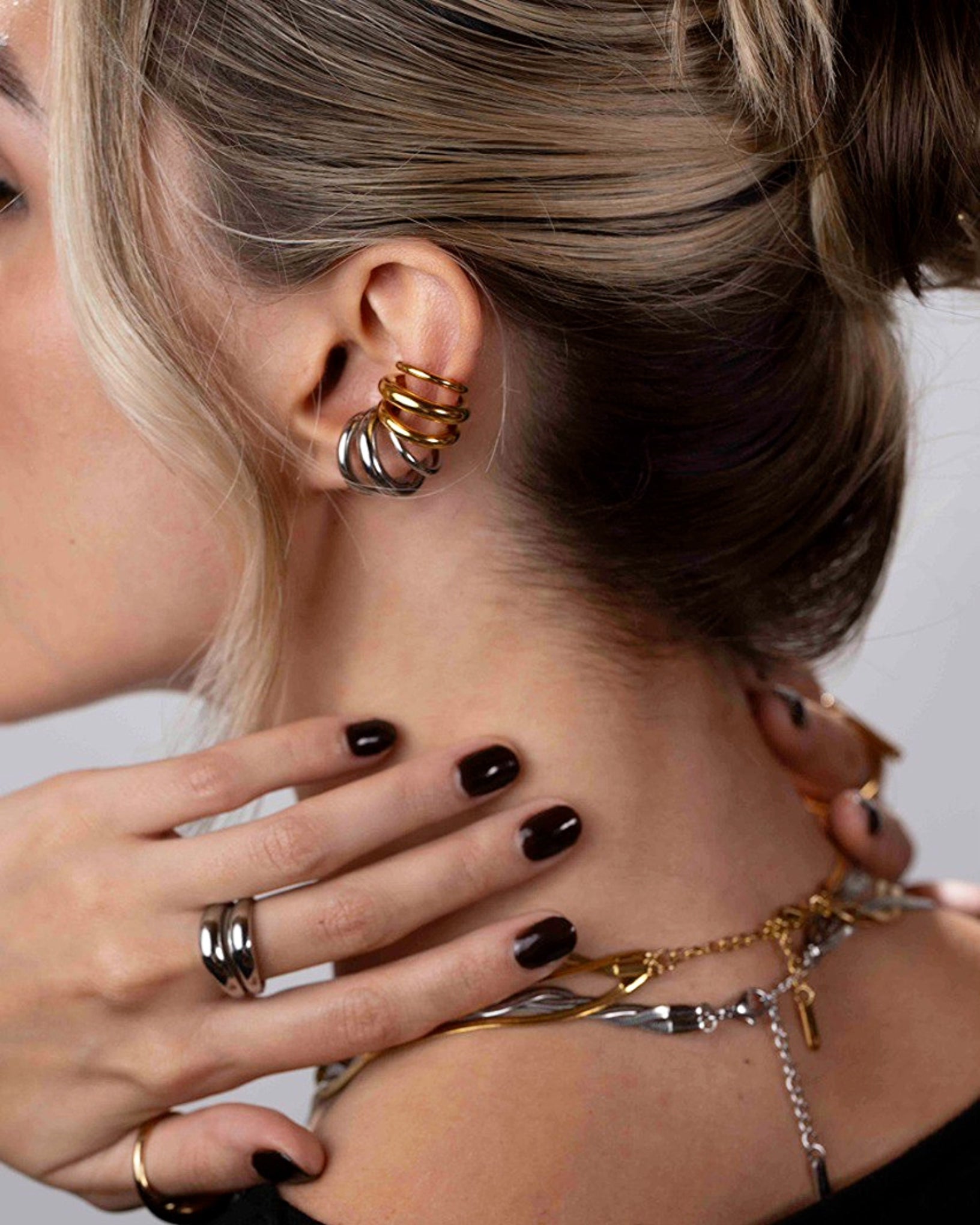 Close-up of a person wearing multiple gold necklaces and rings with a neutral background