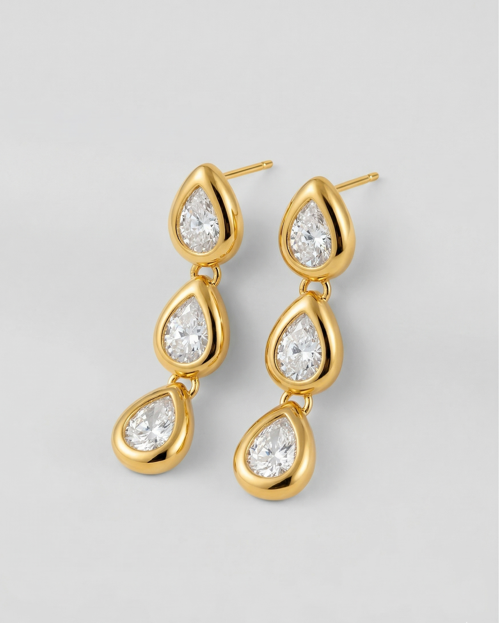 Gold teardrop earrings with clear gemstones on a light gray background