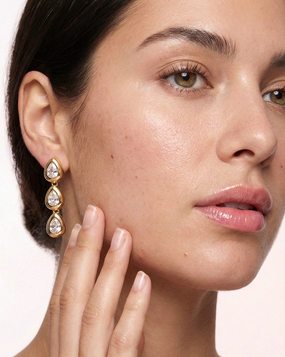 Close-up of a woman wearing gold earrings with clear stones on a white background