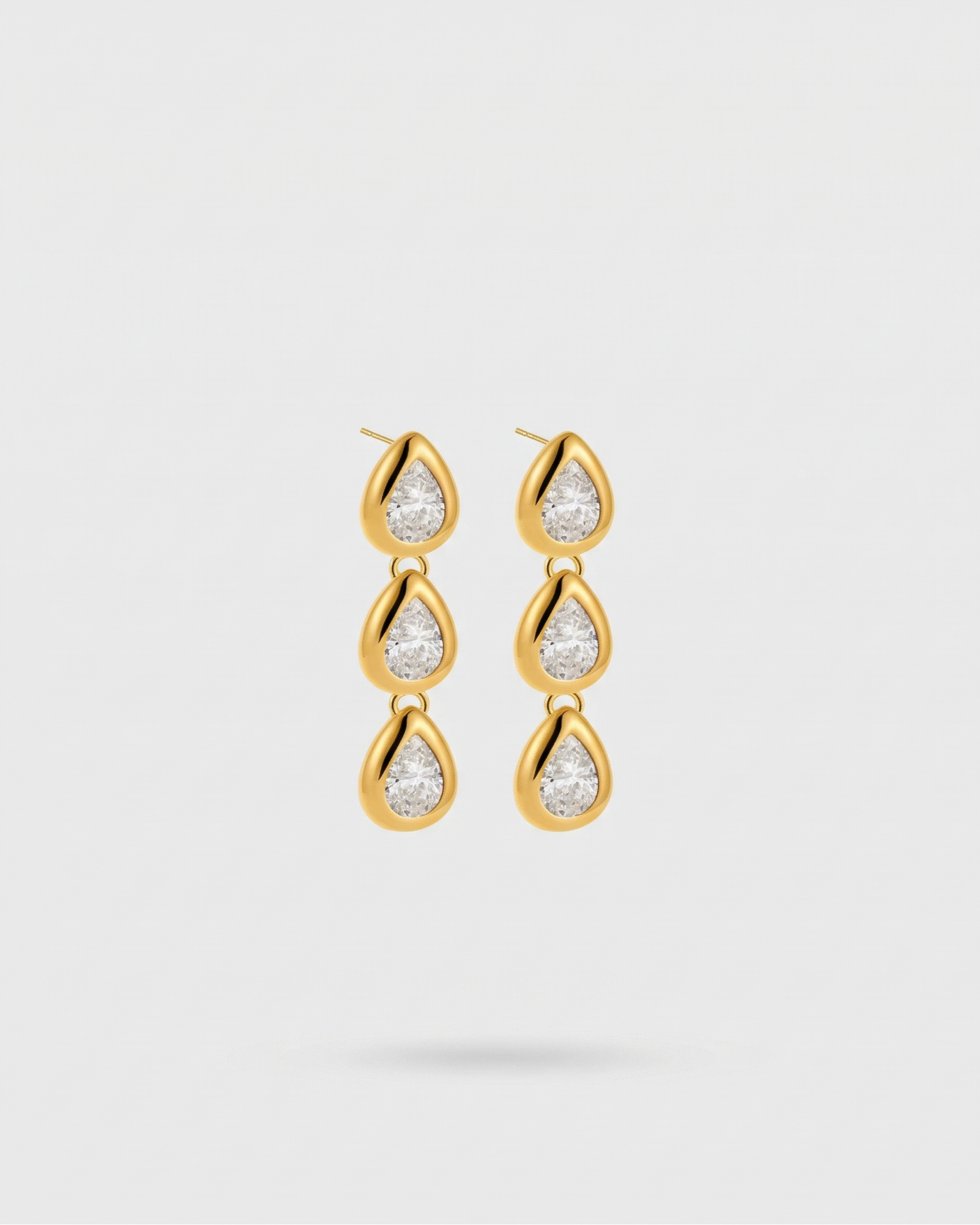 Gold teardrop earrings with clear gemstones on a light gray background