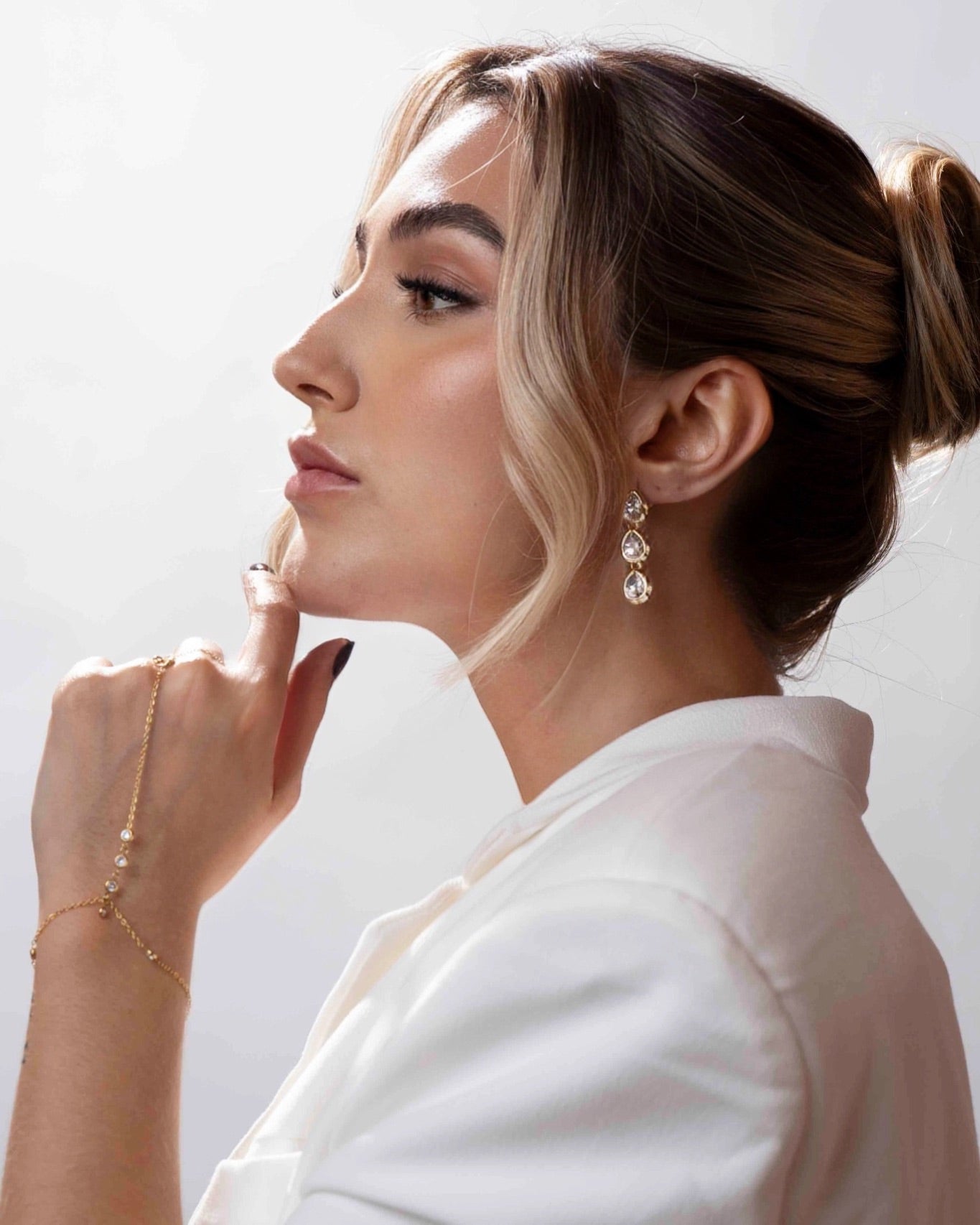 Woman wearing elegant jewelry including earrings, bracelet, and ring on a light background