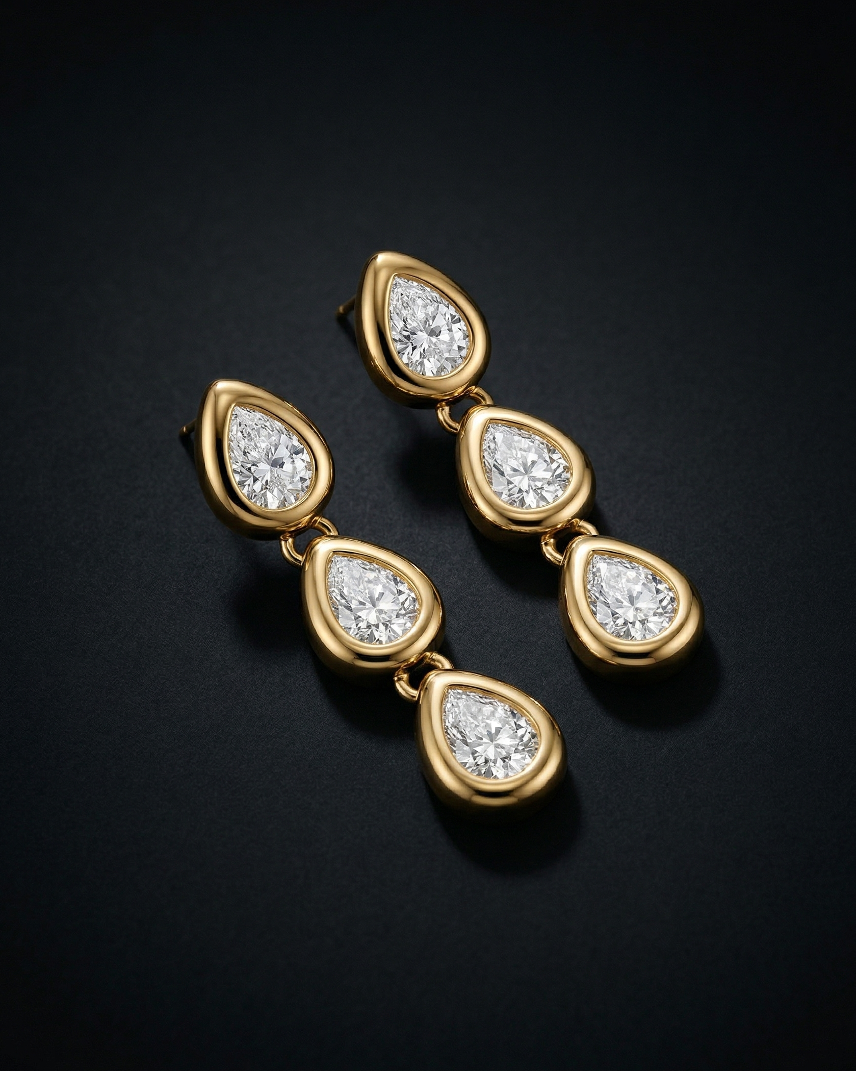 Gold earrings with teardrop-shaped diamonds on a black background