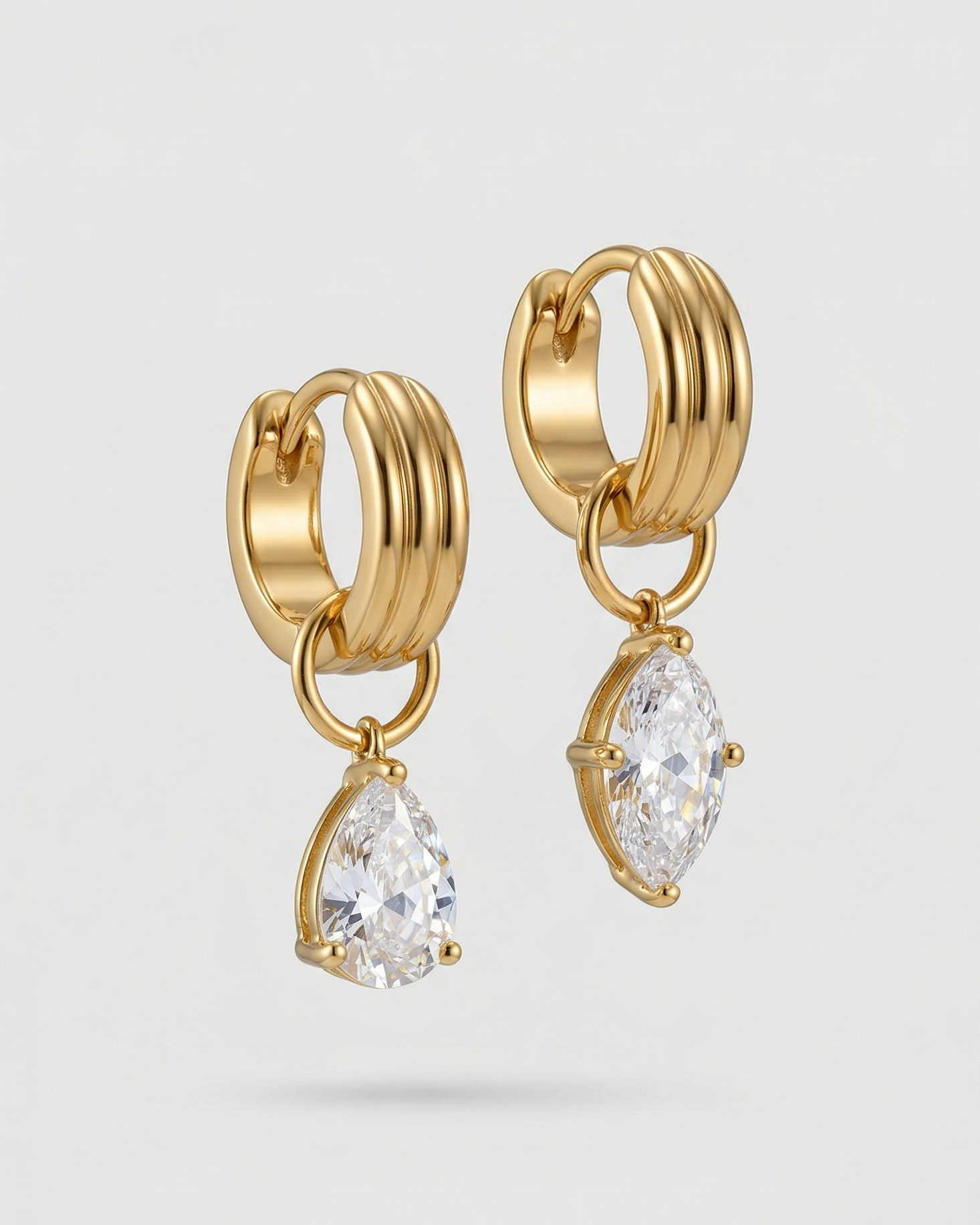 Gold hoop earrings with clear gemstones on a light gray background