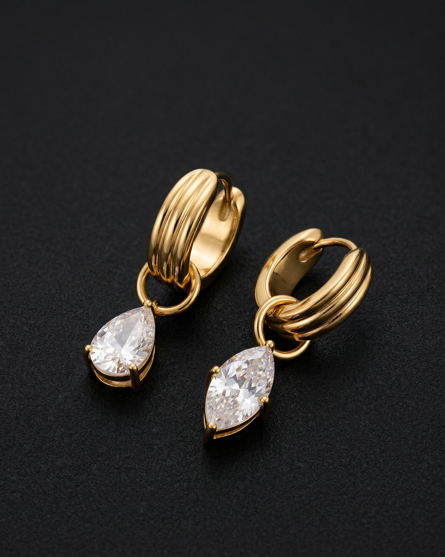 Gold hoop earrings with teardrop-shaped crystals on a black background