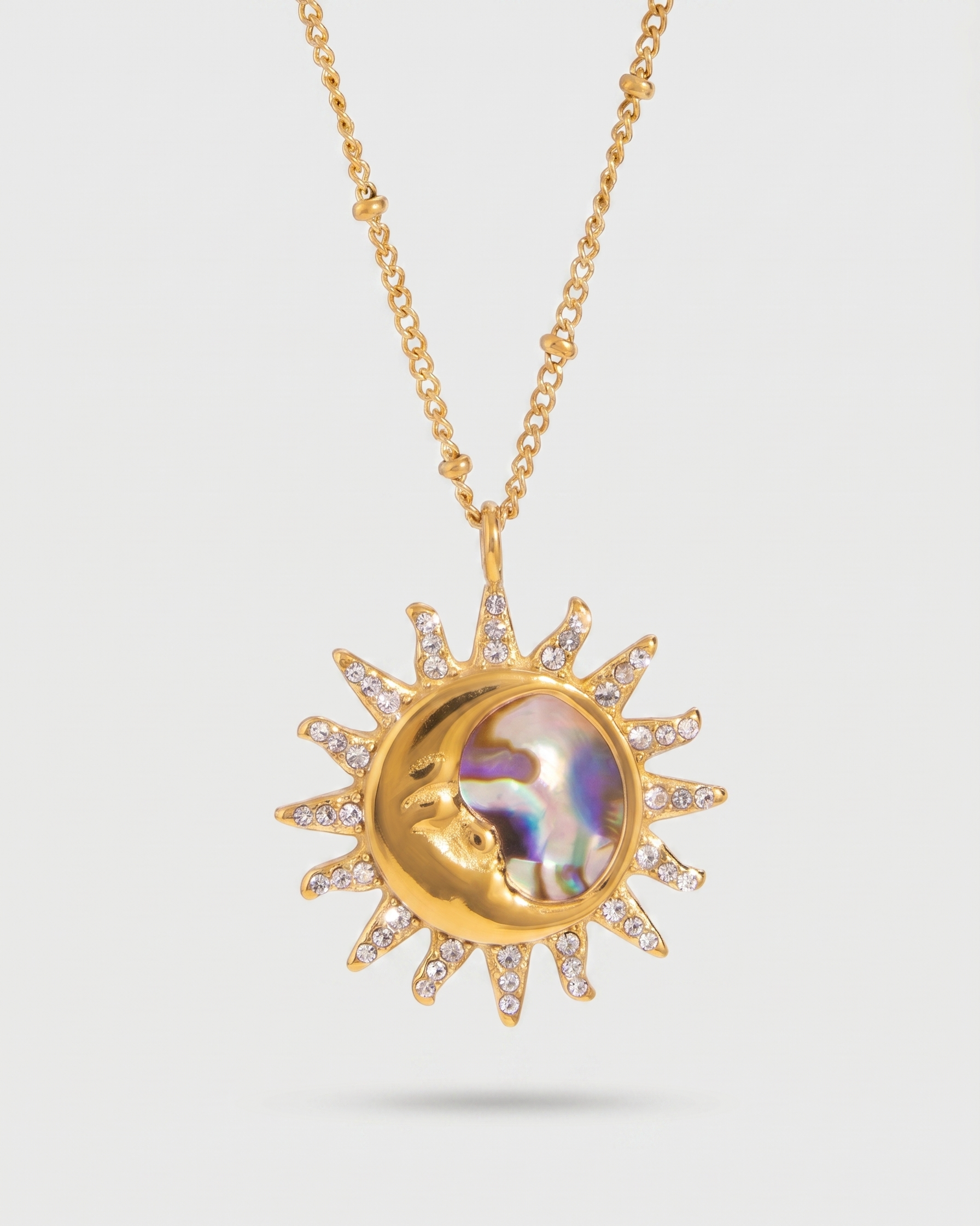 Gold necklace with a sun-shaped pendant featuring a moon design on a light gray background