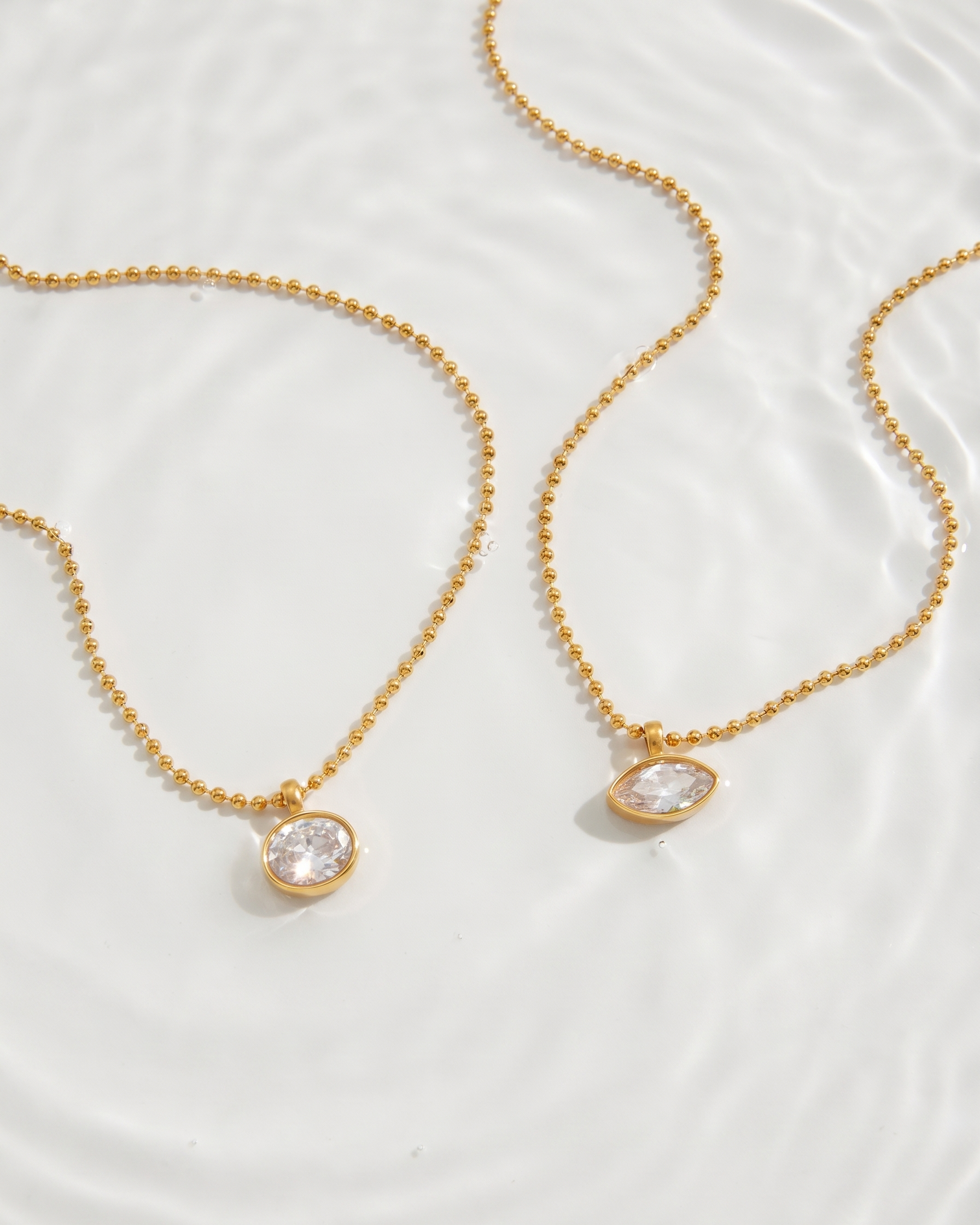Two gold necklaces with clear stone pendants on a white background