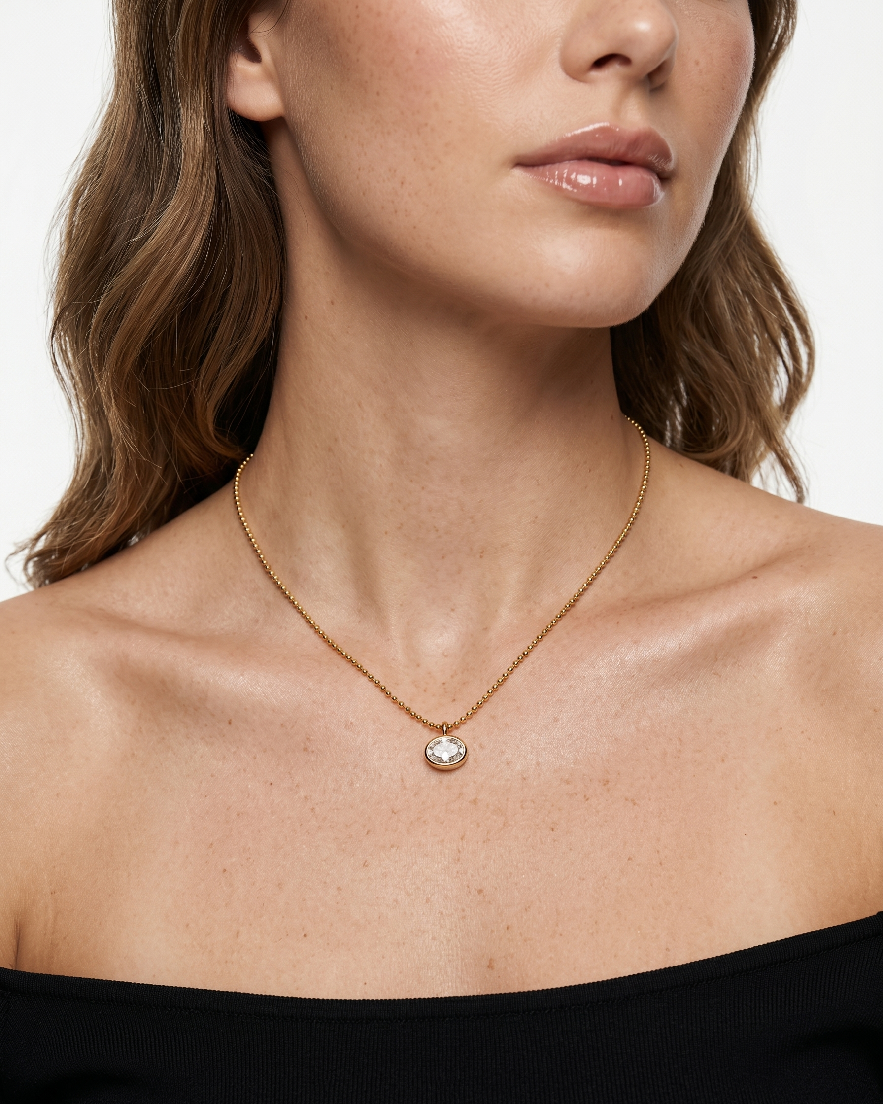 Close-up of a woman wearing a gold necklace with a pendant against a neutral background