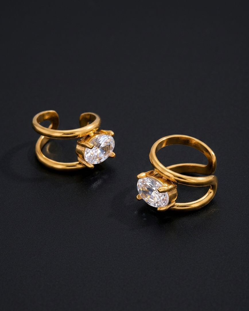 Pair of gold ear cuffs with clear gemstones on a black background