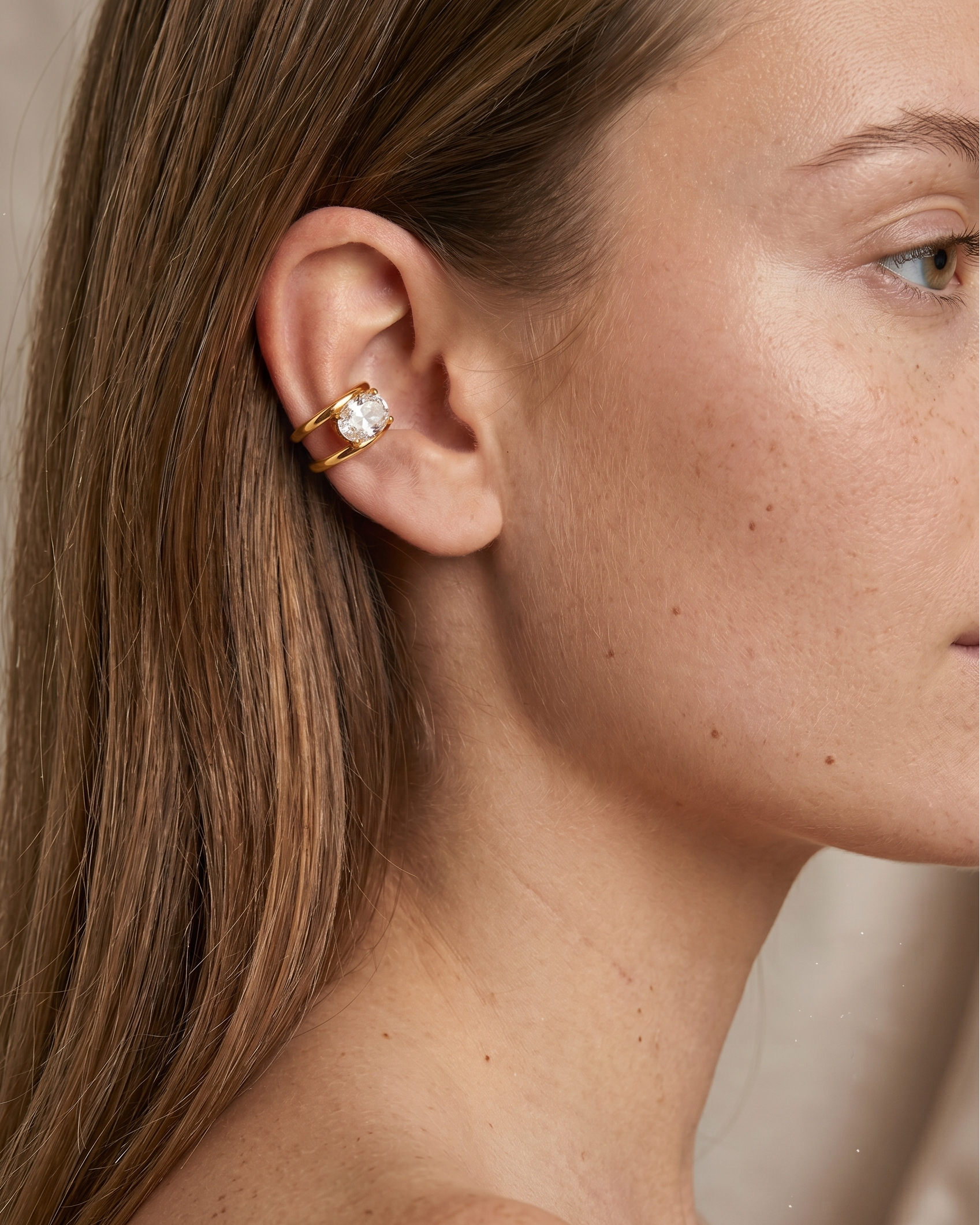 Close-up of a woman's ear wearing a gold earring with a clear gemstone.