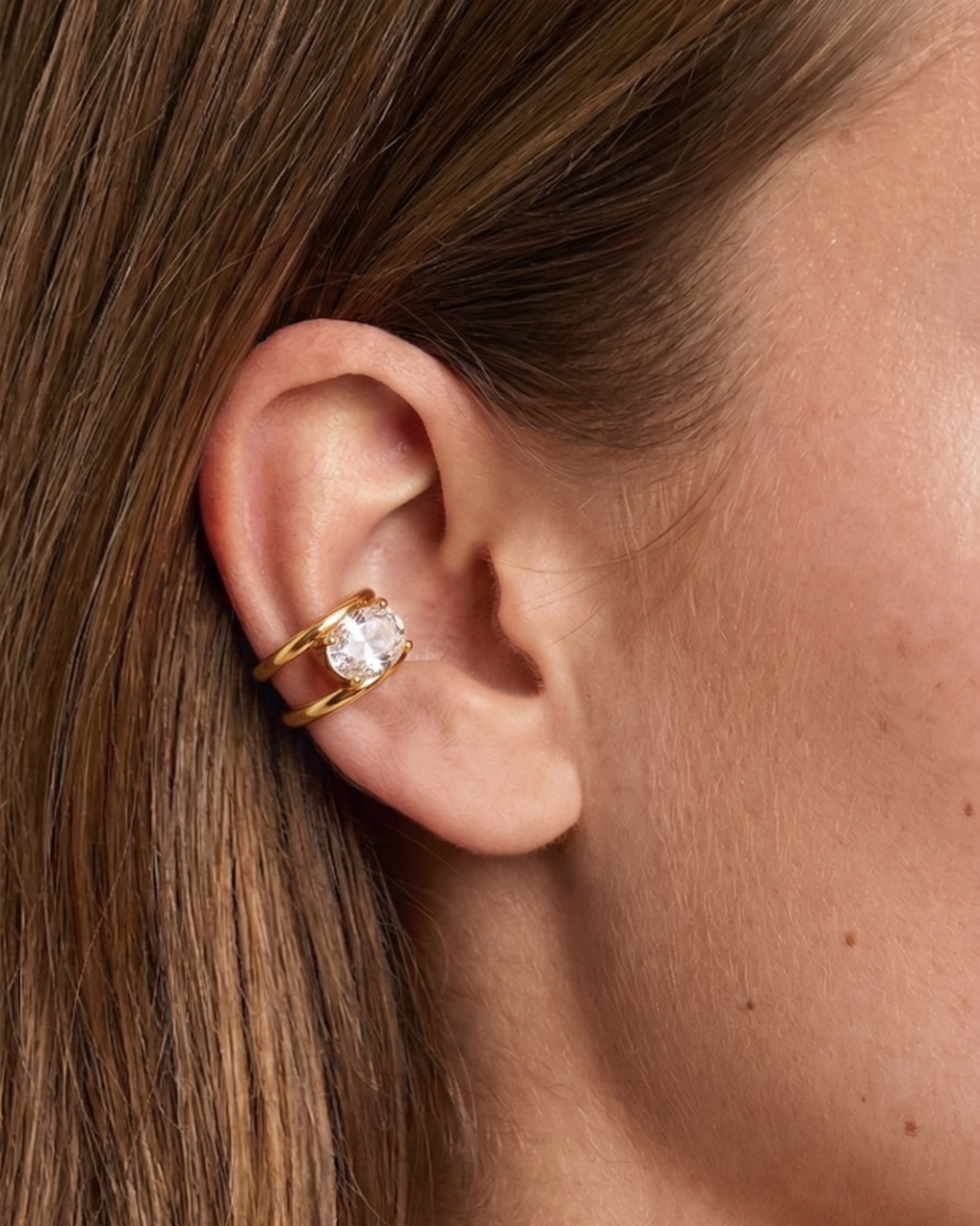 Close-up of an ear wearing a gold earring with a clear gemstone.