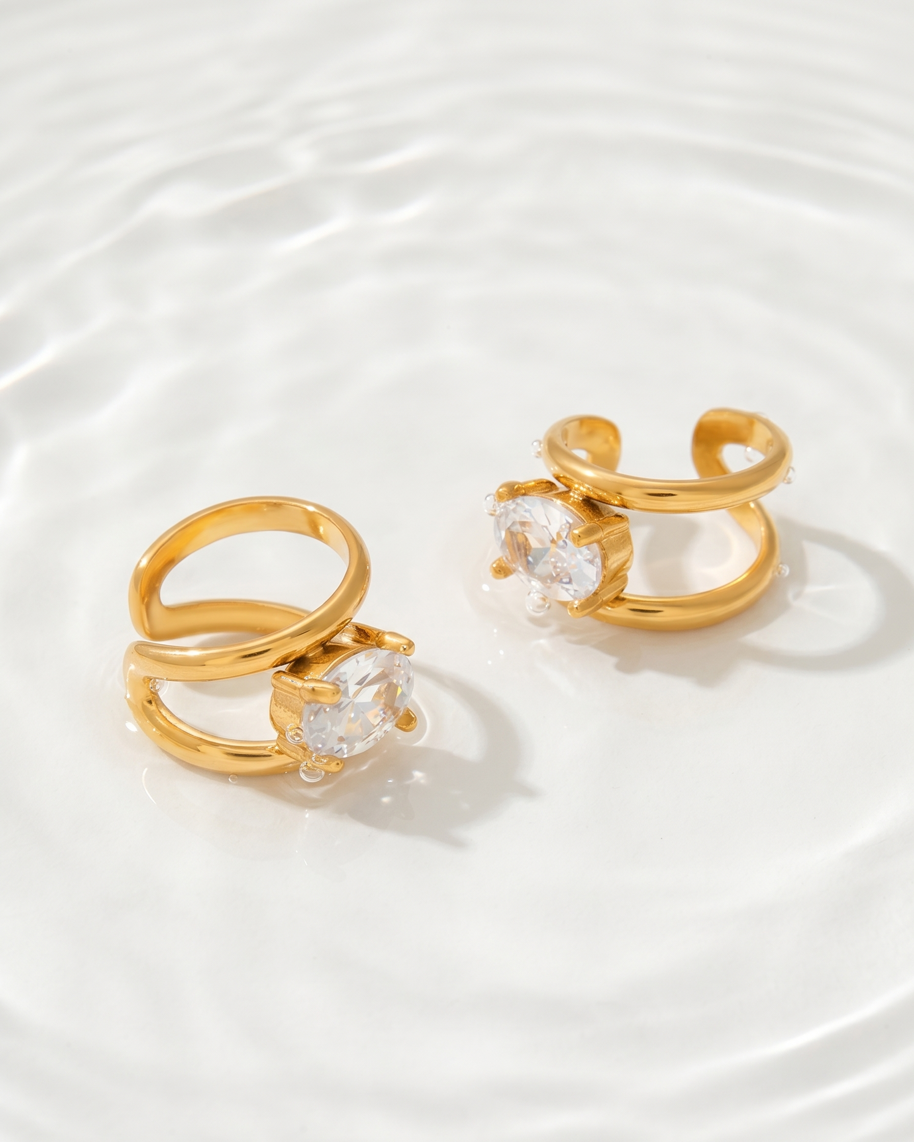 Two gold rings with clear gemstones on a white background